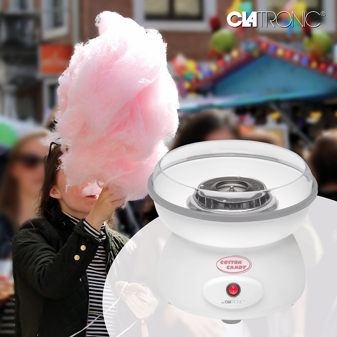 Una máquina de algodón de azúcar blanca y una mujer sosteniendo algodón de azúcar rosa en un carnaval borroso.