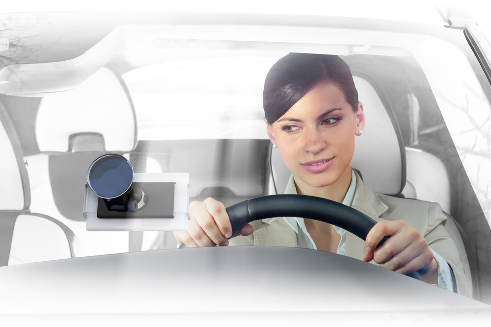 Eine Frau in einem Auto hält das Lenkrad, ein Gerät ist an der Windschutzscheibe befestigt.