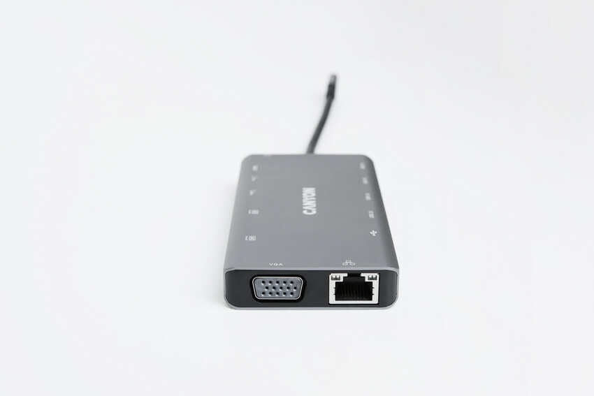 Szary hub USB-C Canyon na białej powierzchni, z portami VGA i Ethernet z przodu.