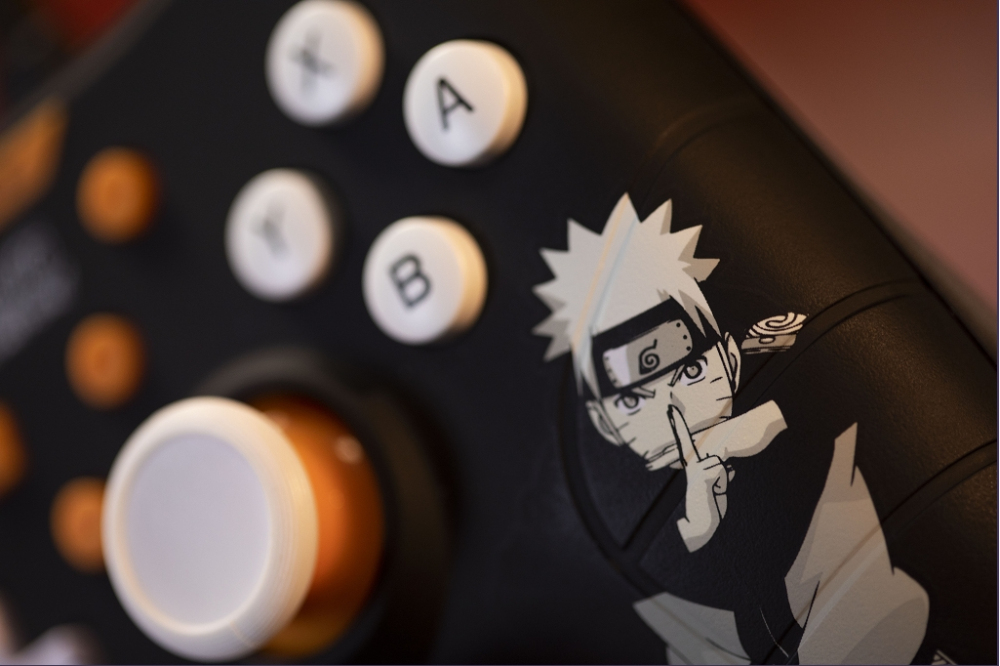 Un mando negro con botones blancos, un joystick blanco y una pegatina de Naruto.