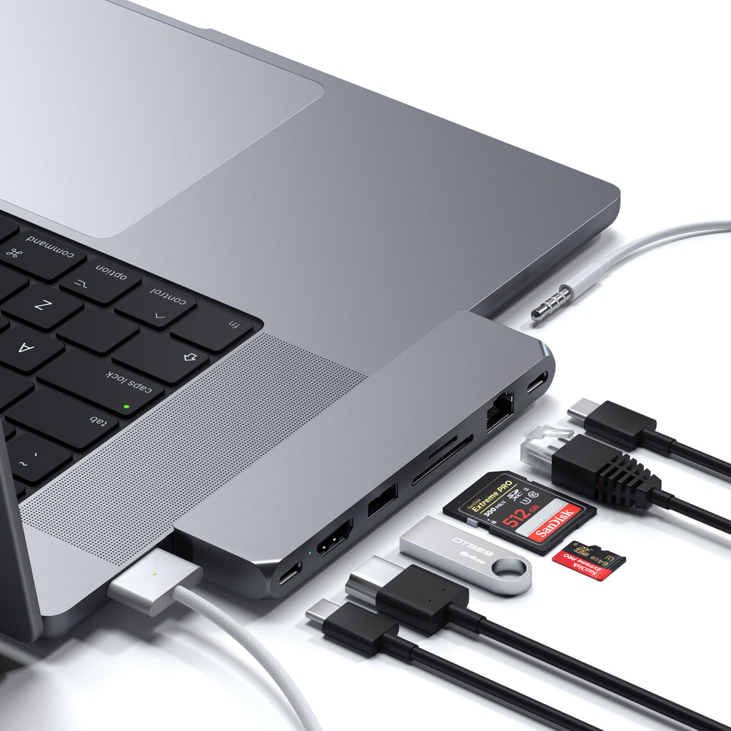 Laptop grigio con hub collegato a cavi, schede SD e chiavette USB su sfondo bianco.