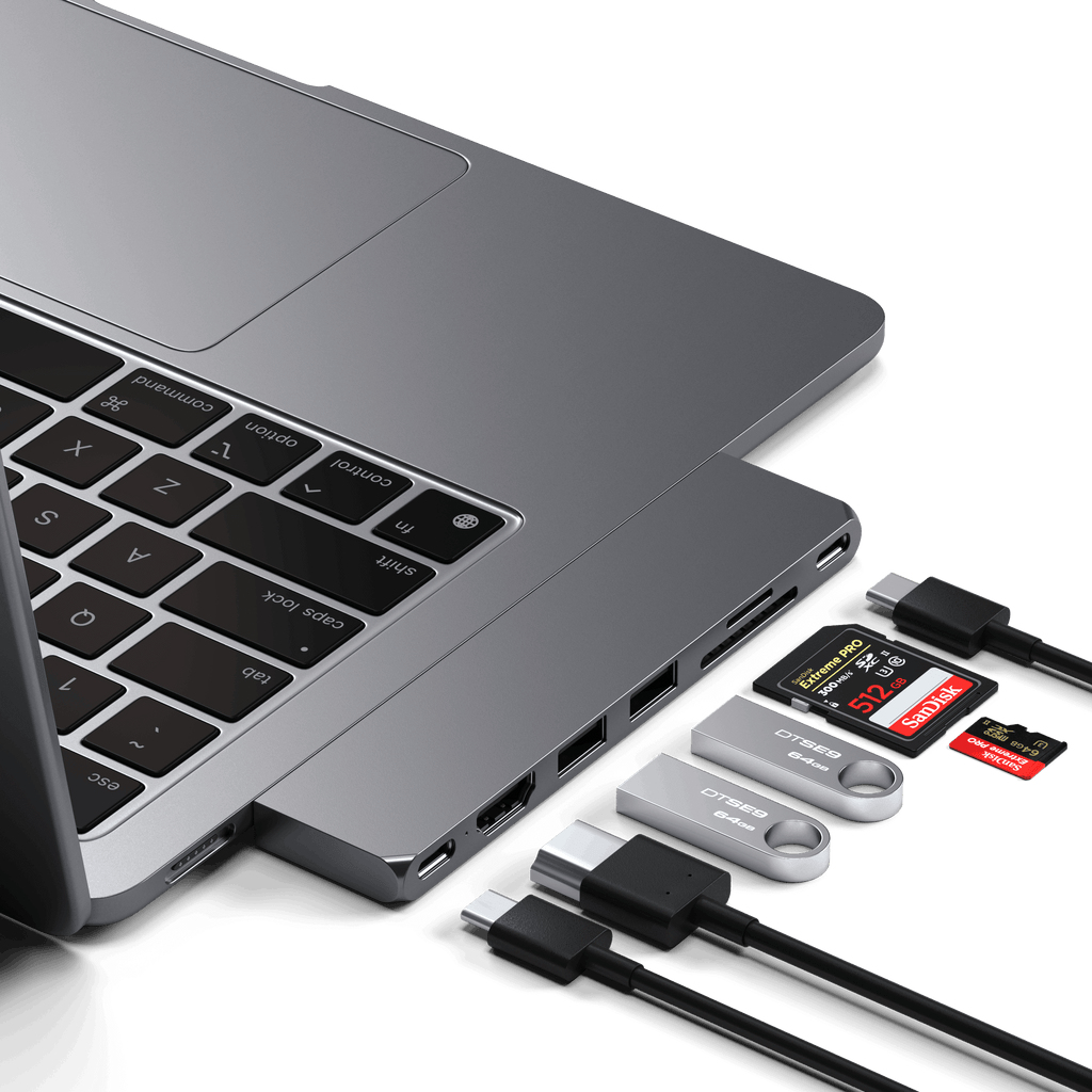 Szary laptop z podłączonym hubem USB-C, pendrivami, kartami SD i kablami na białym tle.