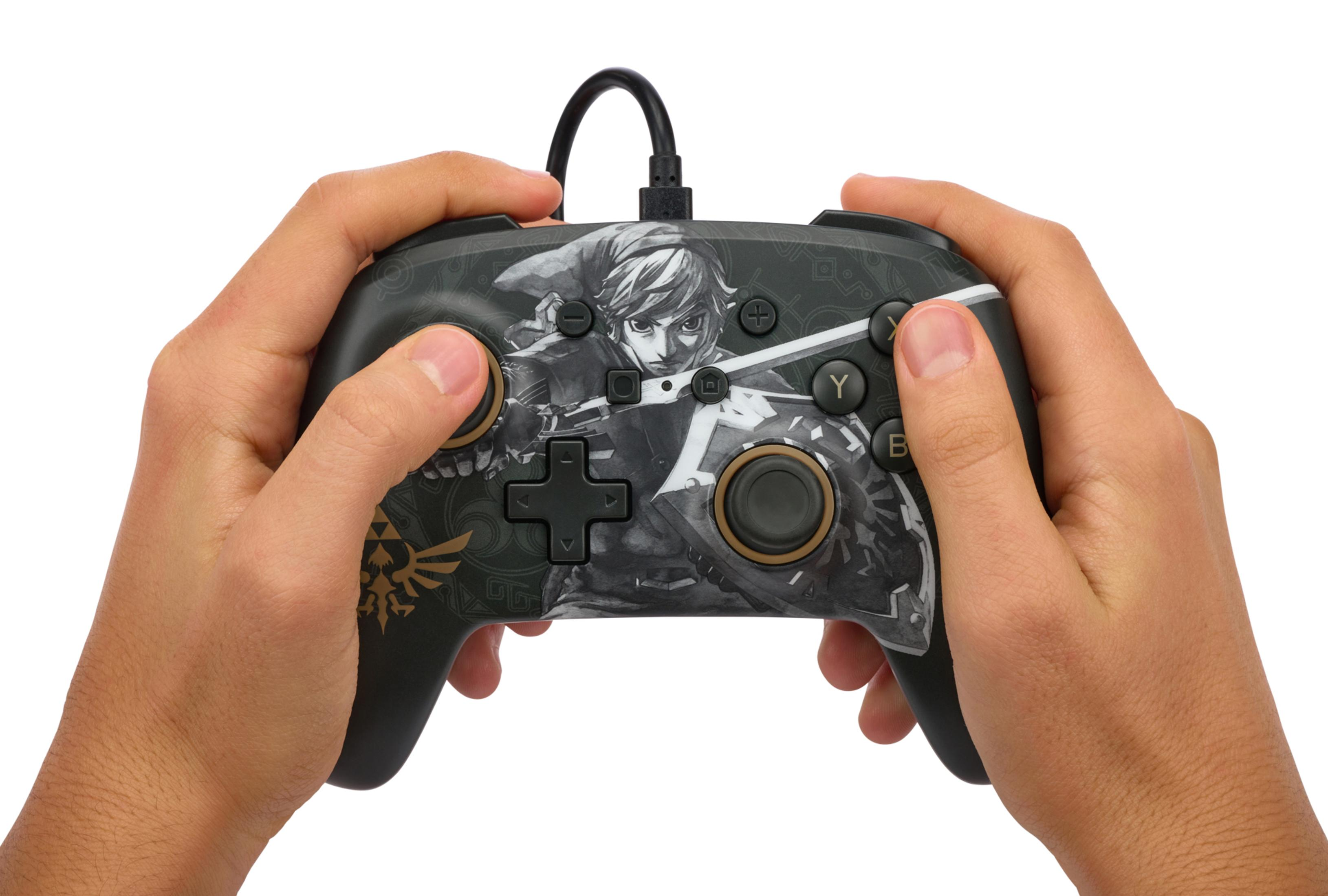 Mani che tengono un controller nero a tema Zelda con grafica di Link su sfondo bianco.