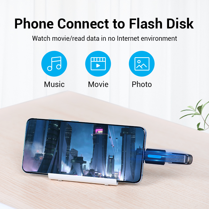 Smartfon na stojaku z podłączoną pendrivem na drewnianym stole, pokazujący ikony muzyki, filmu i zdjęć.