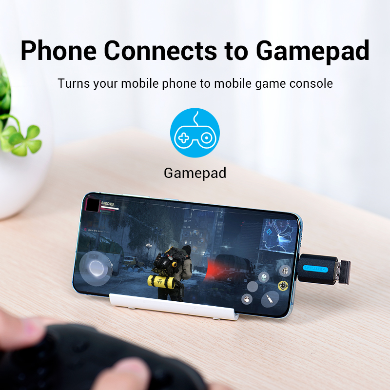 Smartfon na stojaku wyświetla grę, połączony przez adapter, z padem na drewnianym biurku.