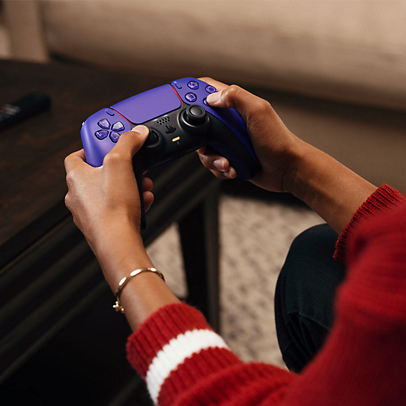 Eine Person in einem roten Pullover hält einen lila und schwarzen Controller.