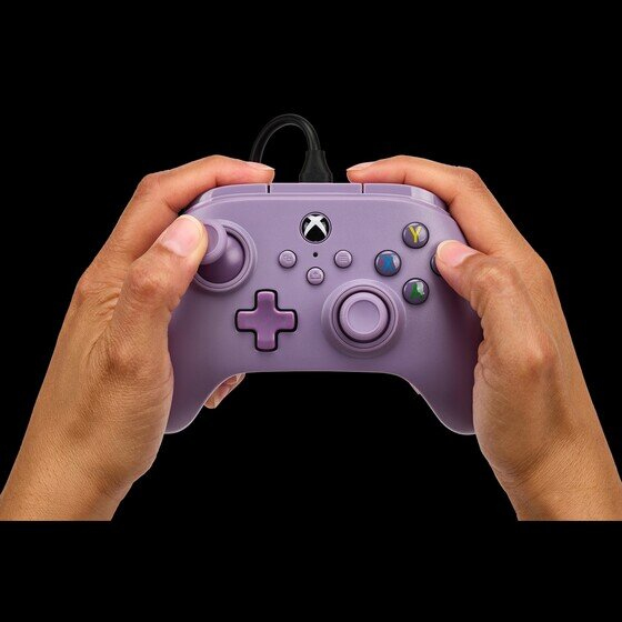Dwie dłonie trzymają jasnofioletowy kontroler Xbox z czarnym kablem na czarnym tle.