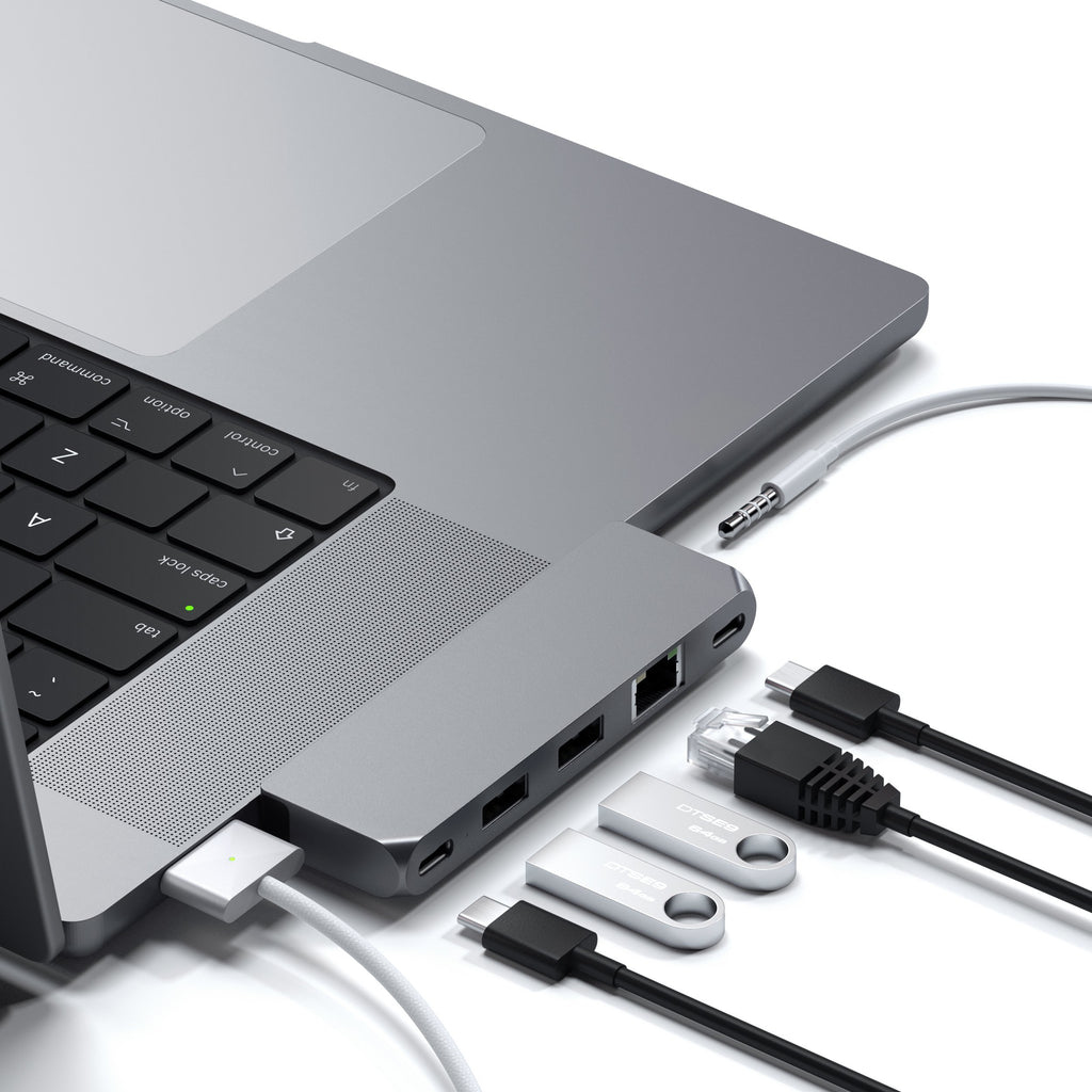 Portátil gris con concentrador USB-C conectado, cables y memorias USB sobre fondo blanco.