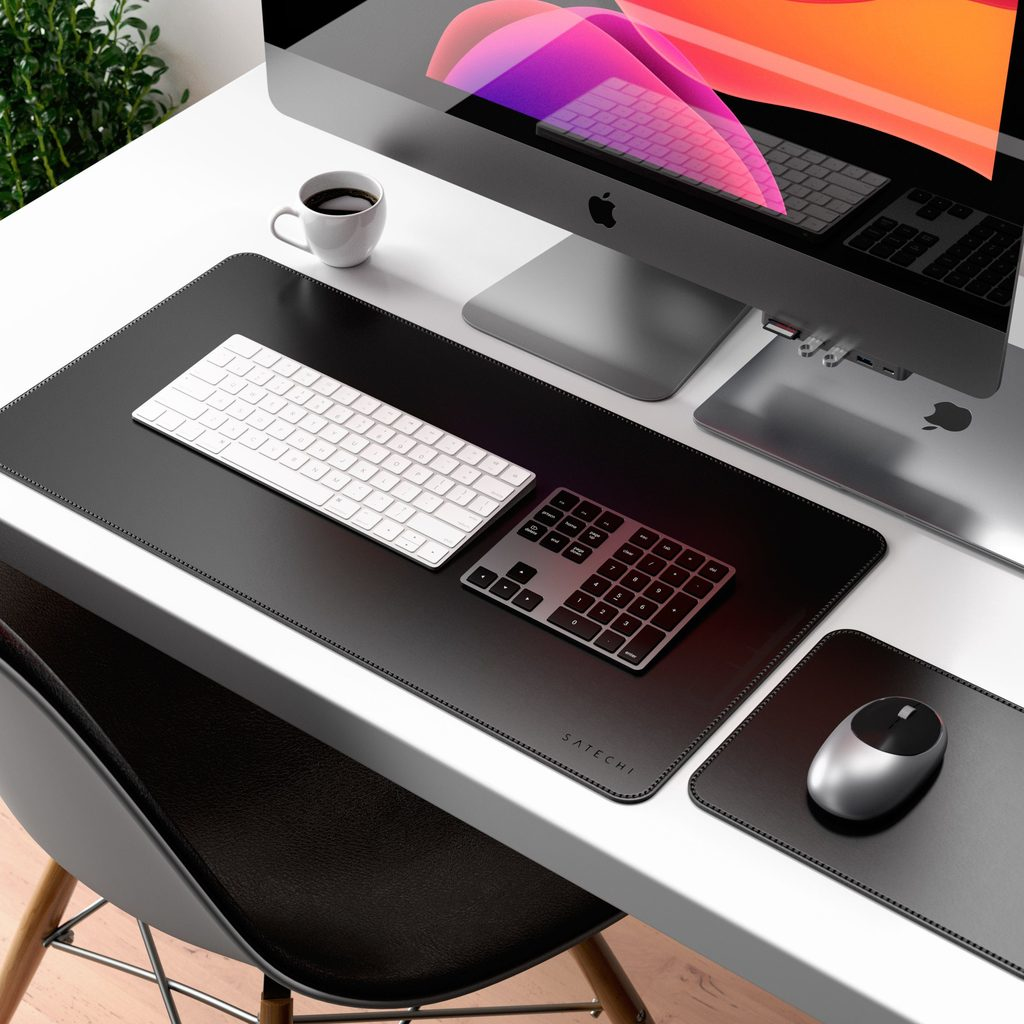 Un escritorio blanco con alfombrilla negra, teclado blanco, teclado numérico, ordenador y taza de café.