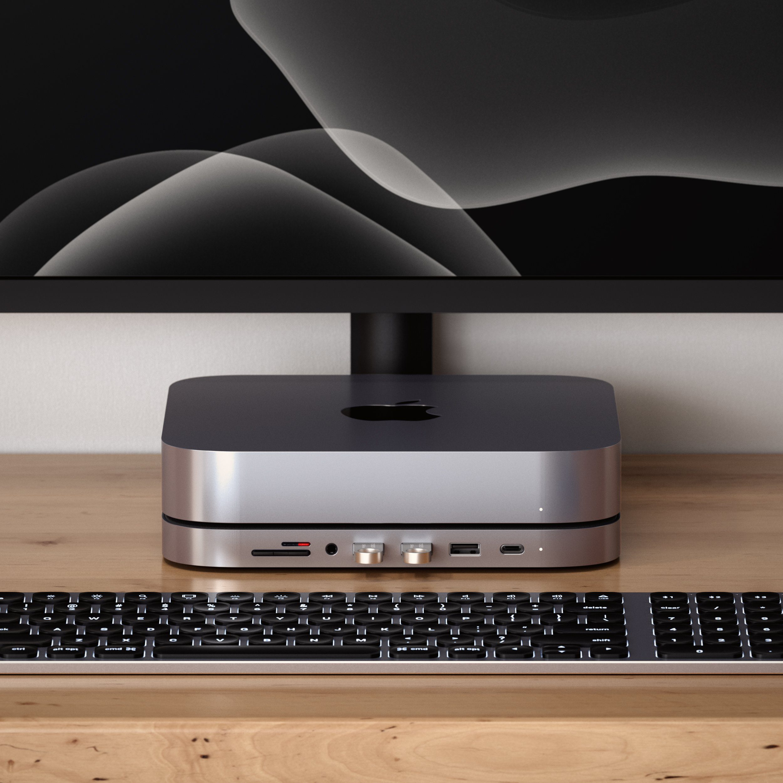 Mac mini stoi na drewnianym biurku pod monitorem, z klawiaturą z przodu i podłączonym hubem.