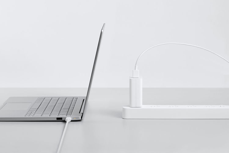 Ein silberner Laptop ist über ein weißes Kabel an eine Steckdosenleiste angeschlossen, auf weißem Hintergrund.