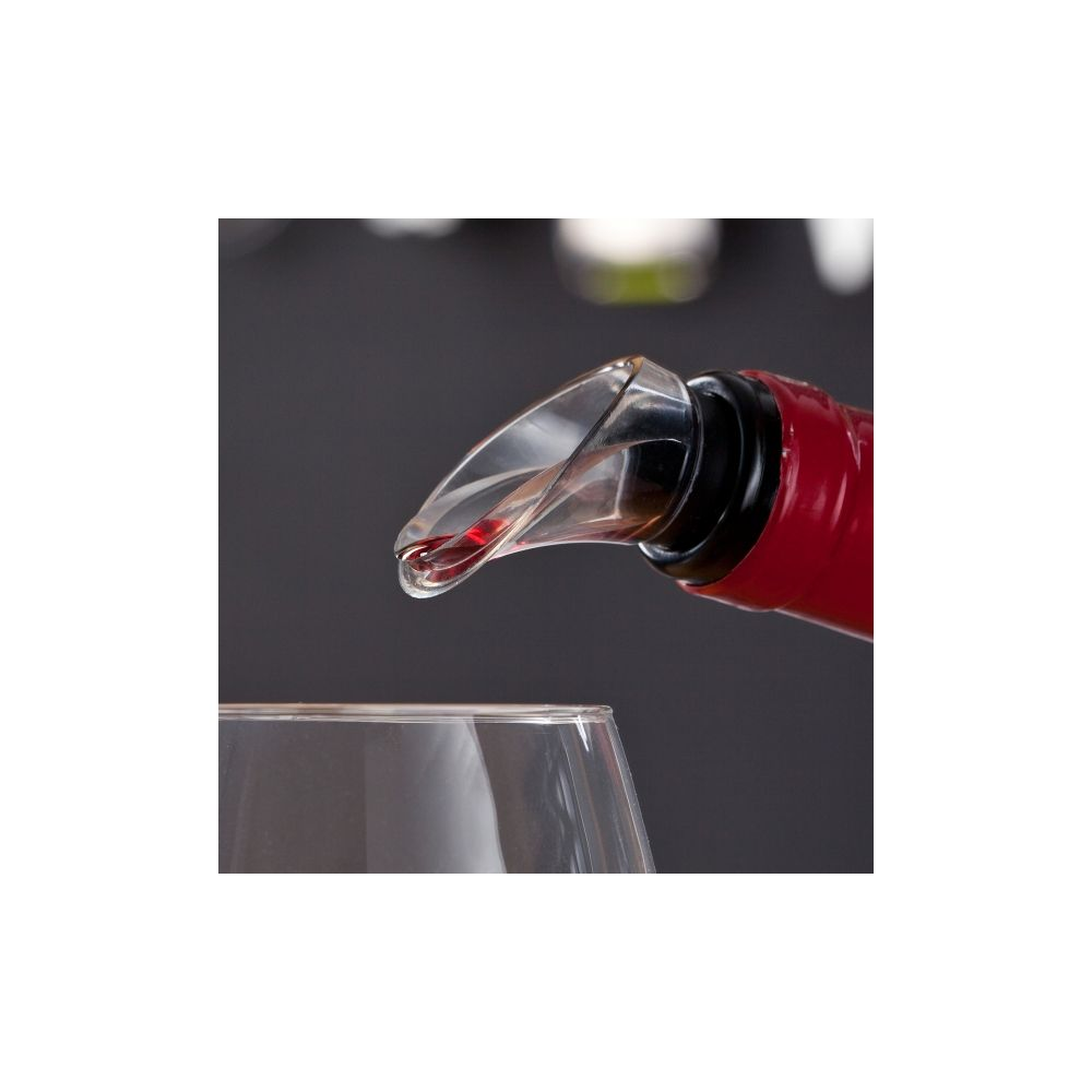 Un versatore di vino trasparente in una bottiglia rossa, sopra un bicchiere vuoto su sfondo scuro.