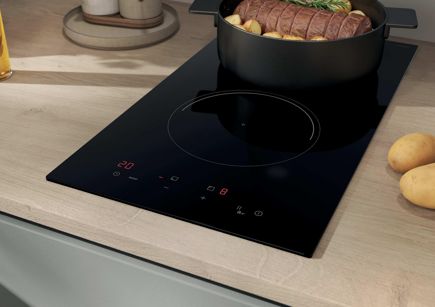 Un piano cottura a induzione nero su un piano di lavoro in legno con una pentola piena di carne e patate.