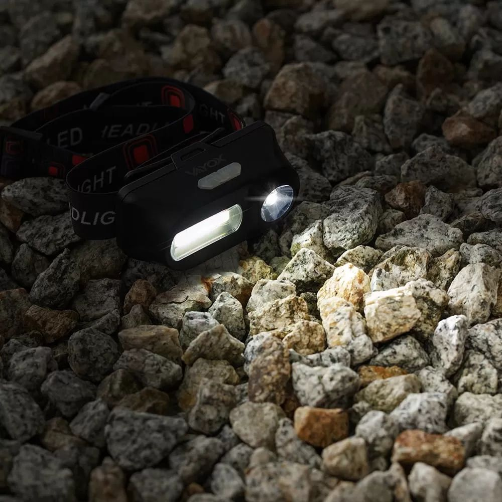 Egy fekete LED-es fejlámpa apró kavicsokon pihen, közvetlenül maga előtt világítva meg a köveket.