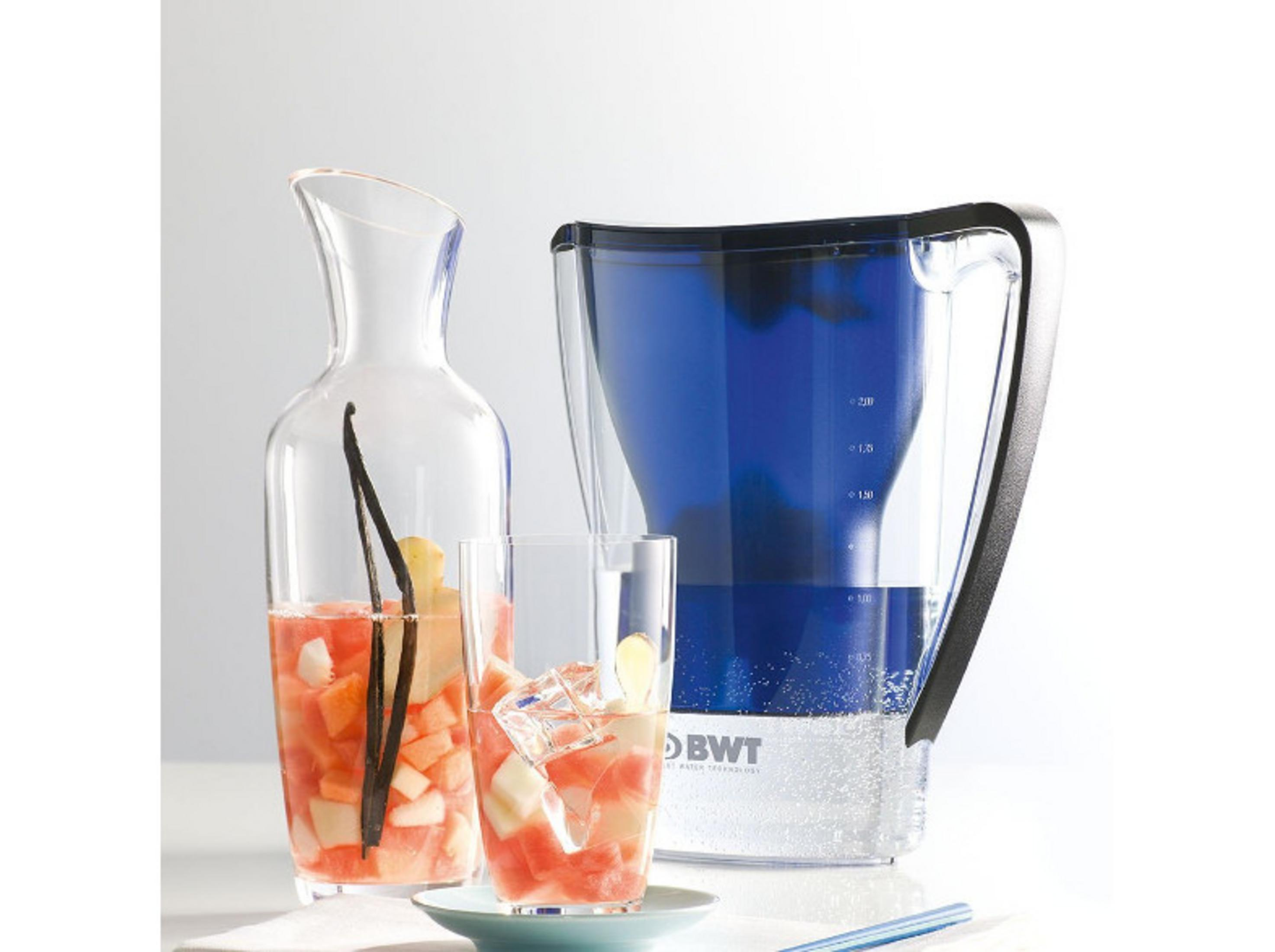 Ein blauer Wasserfilterkrug, eine Glas Karaffe mit Früchten und Vanilleschote und ein gefülltes Glas auf einem Tisch.
