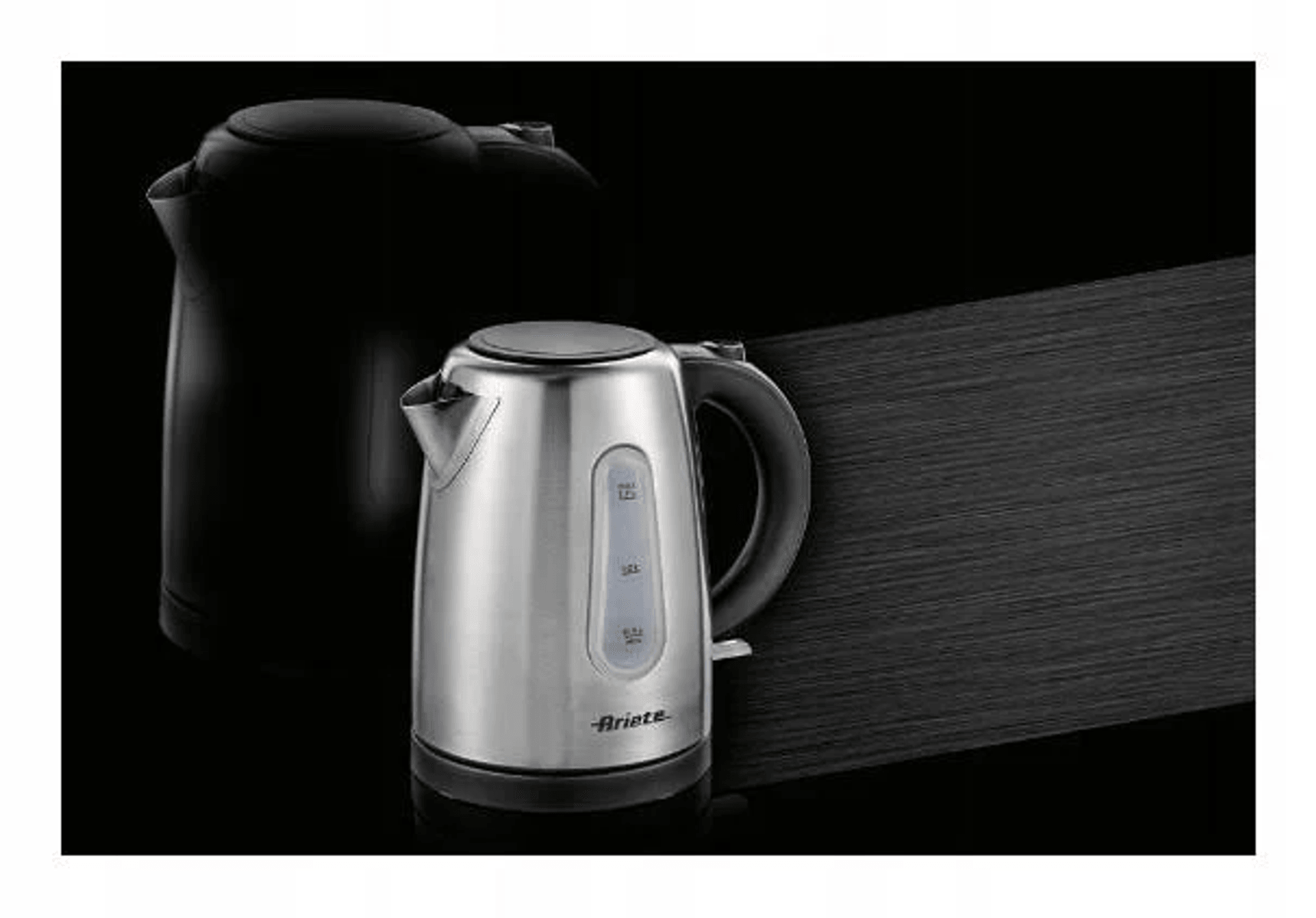 Un hervidor de acero inoxidable plateado en primer plano y un modelo negro detrás sobre fondo oscuro.