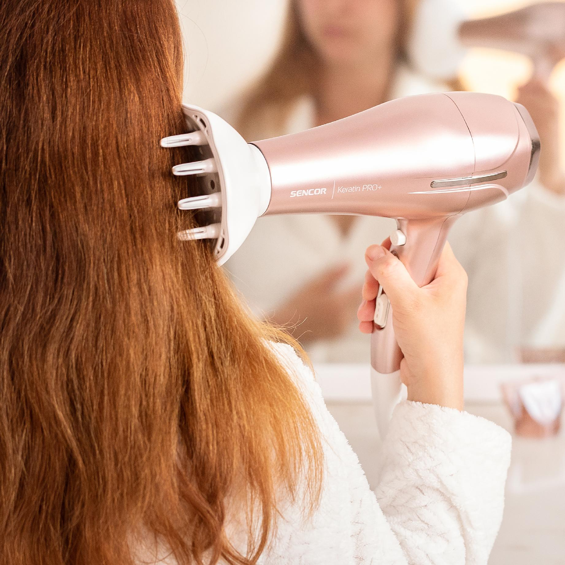Una mujer se seca el pelo en un baño con un secador Sencor de oro rosa.