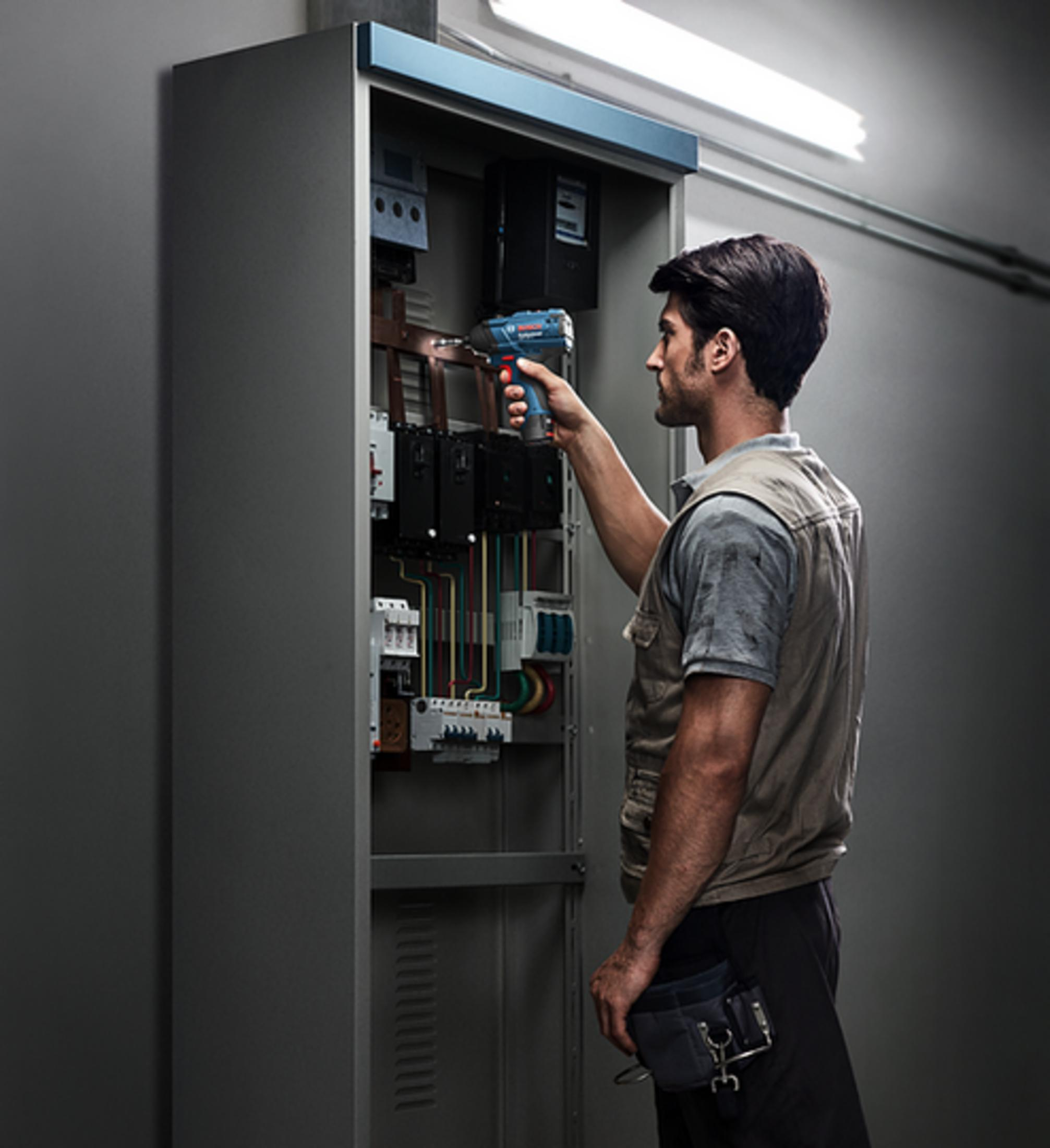 Un tecnico lavora su un quadro elettrico con un utensile blu in una stanza.