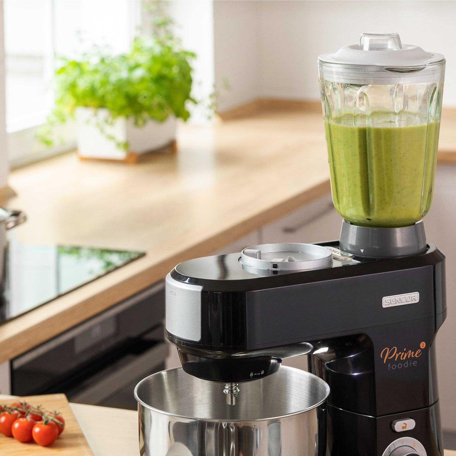 Un robot da cucina nero con un frullato verde nell'accessorio si trova su un piano di lavoro in legno.