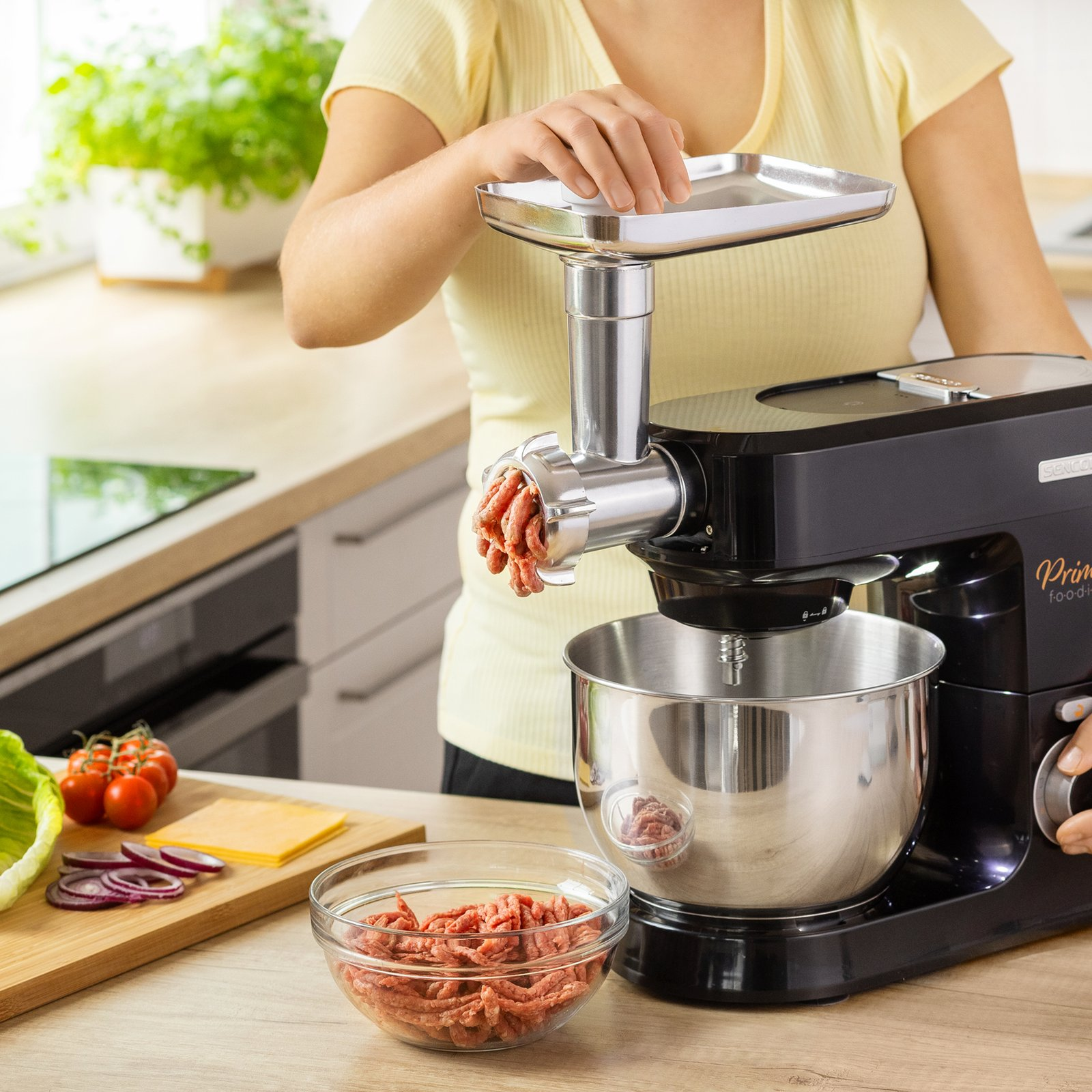 Una donna in maglia gialla usa un robot da cucina nero che estrude carne macinata.