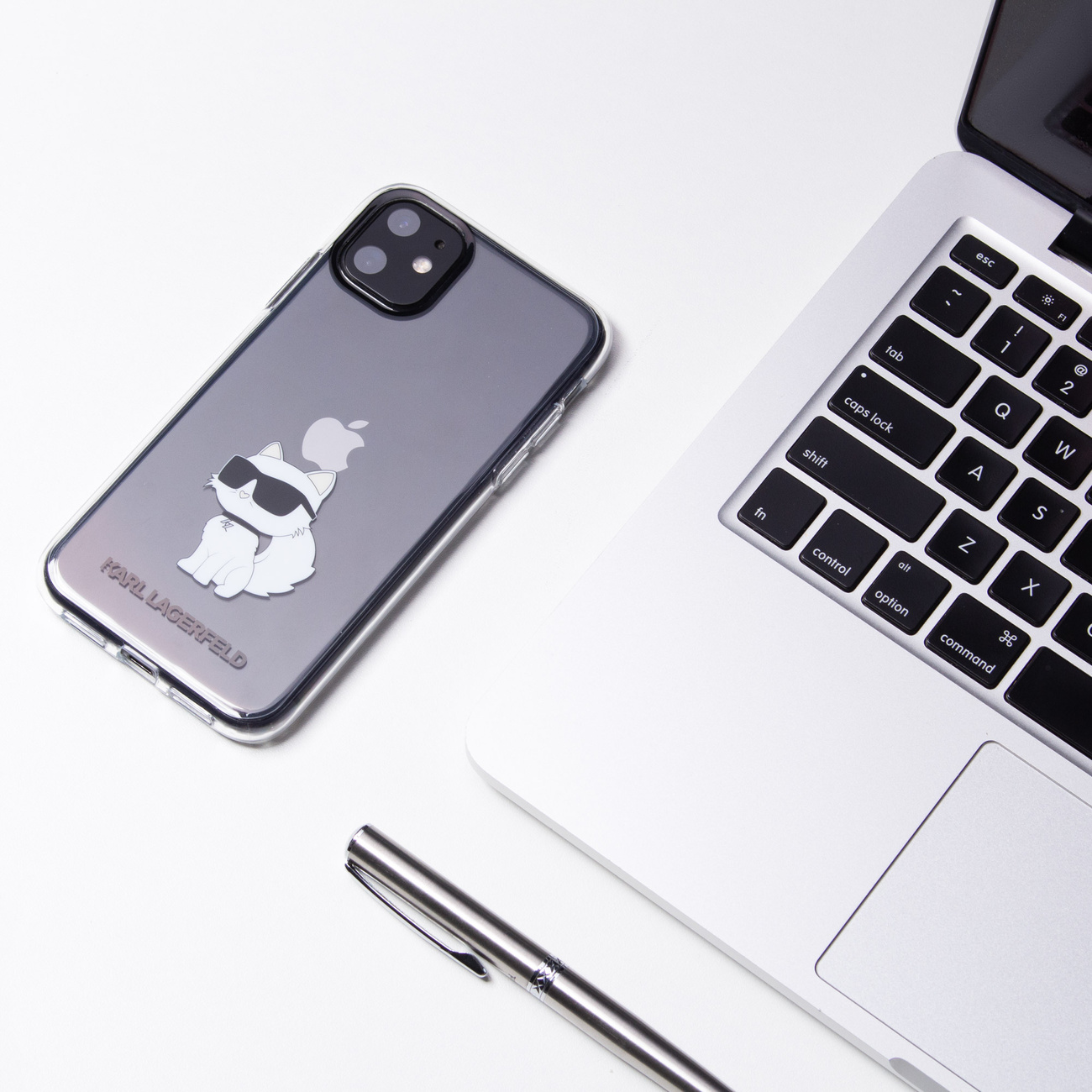 Beyaz bir masada Karl Lagerfeld kedi kılıflı akıllı telefon, dizüstü ve kalem.