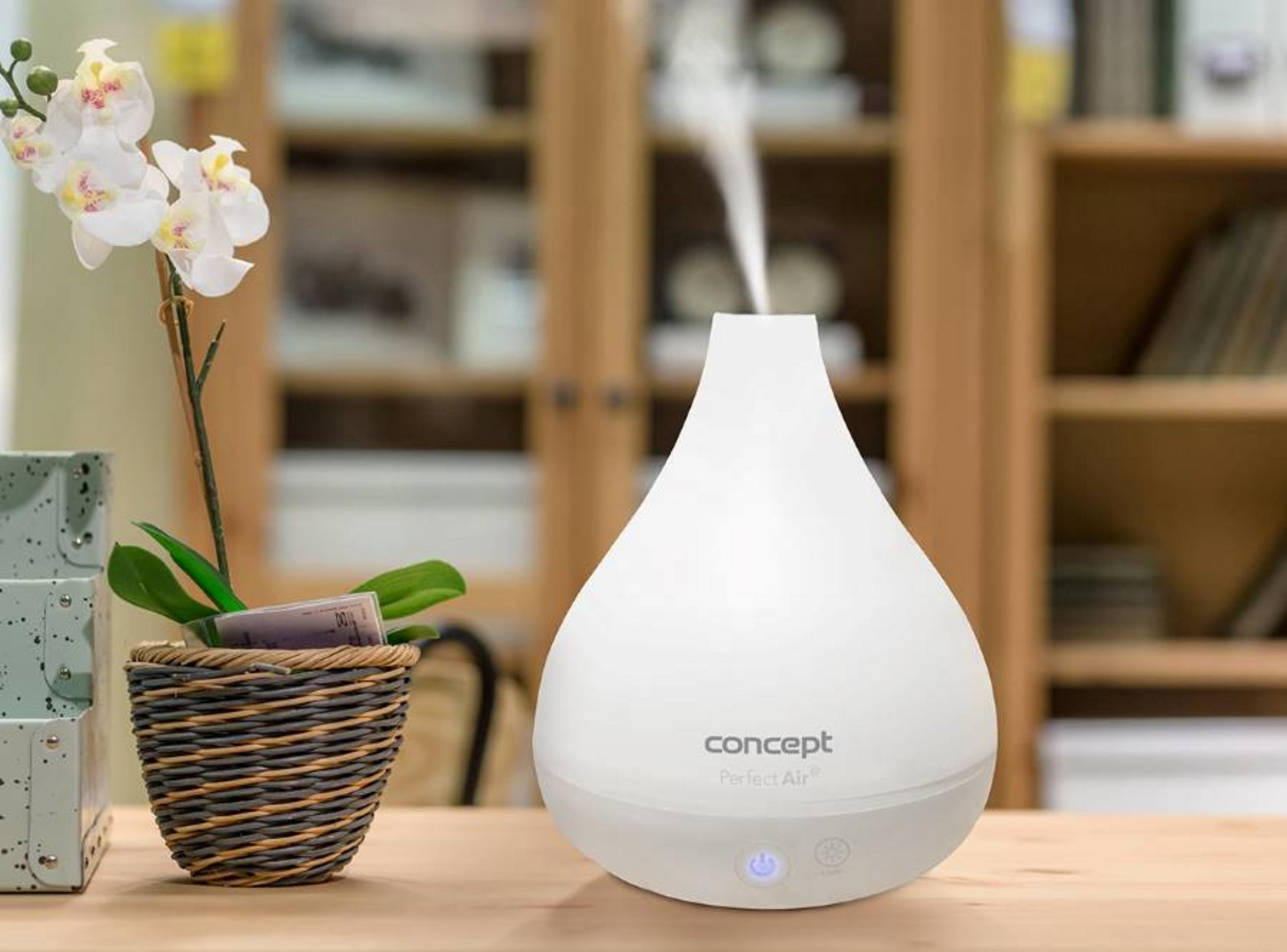 Un difusor de aroma blanco en una mesa de madera emite vapor, junto a una orquídea en maceta.