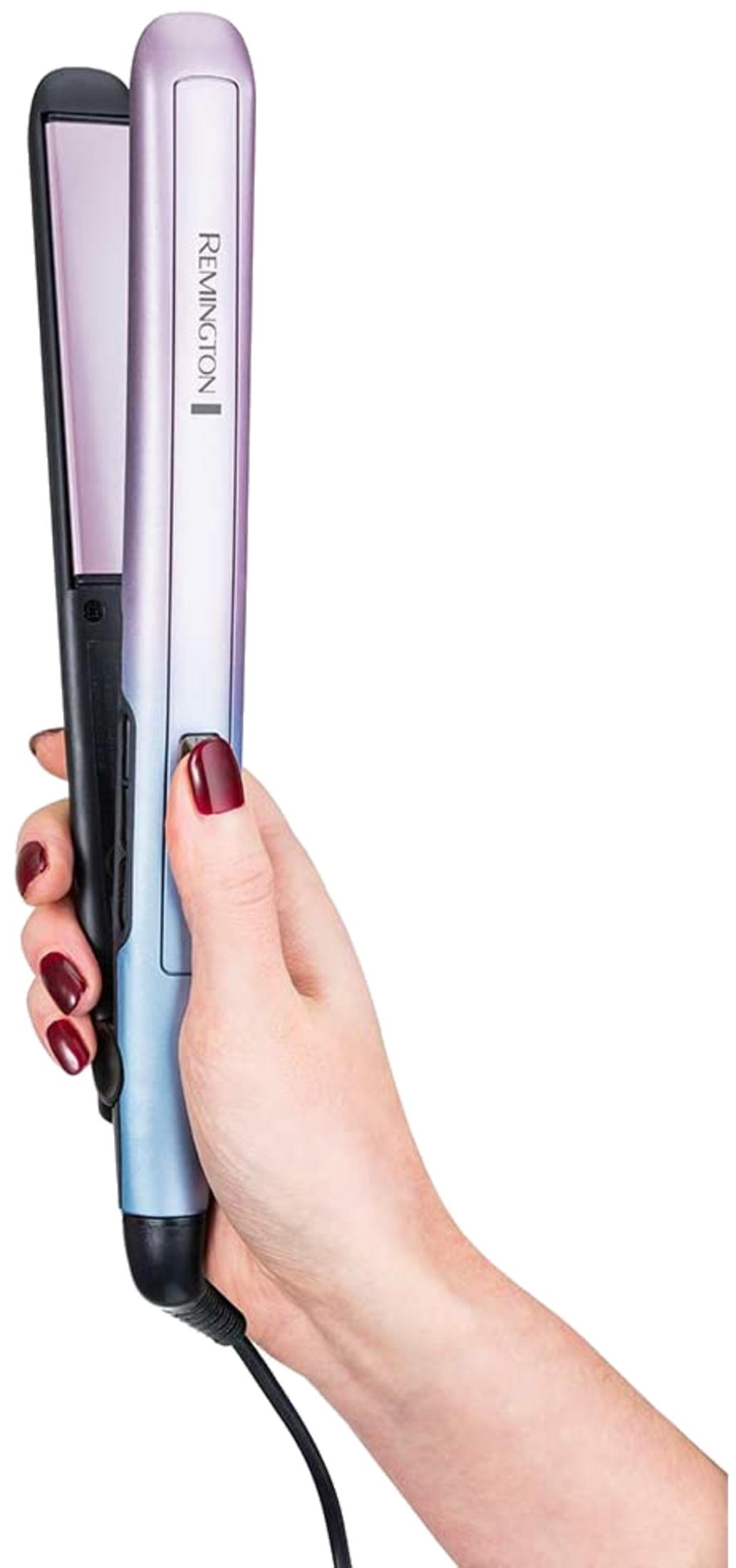 Una mano con esmalte de uñas rojo oscuro sostiene una plancha de pelo Remington azul pastel y morada sobre fondo blanco.