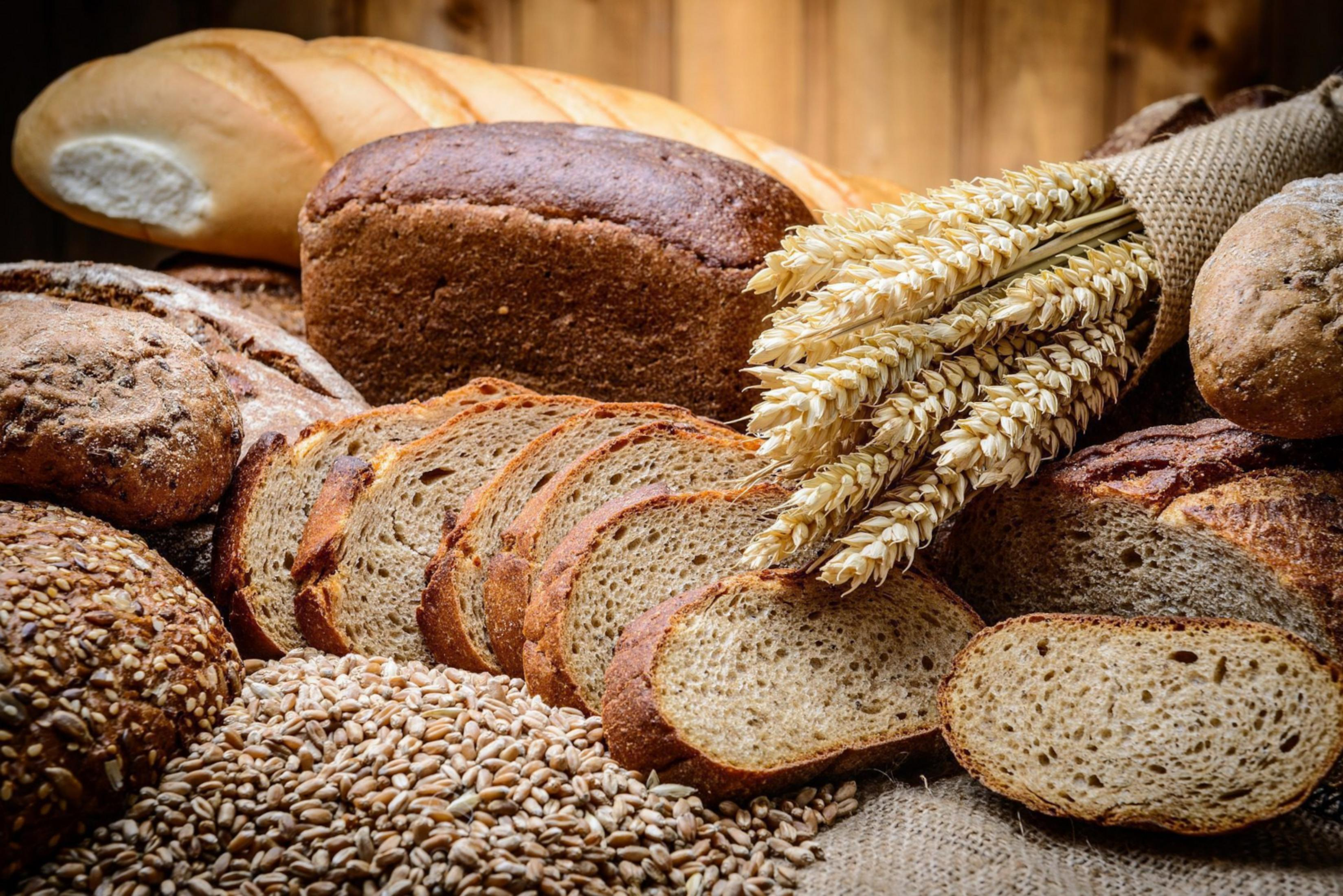 Varietà di pani, pagnotte affettate e spighe di grano su un sacco di juta.
