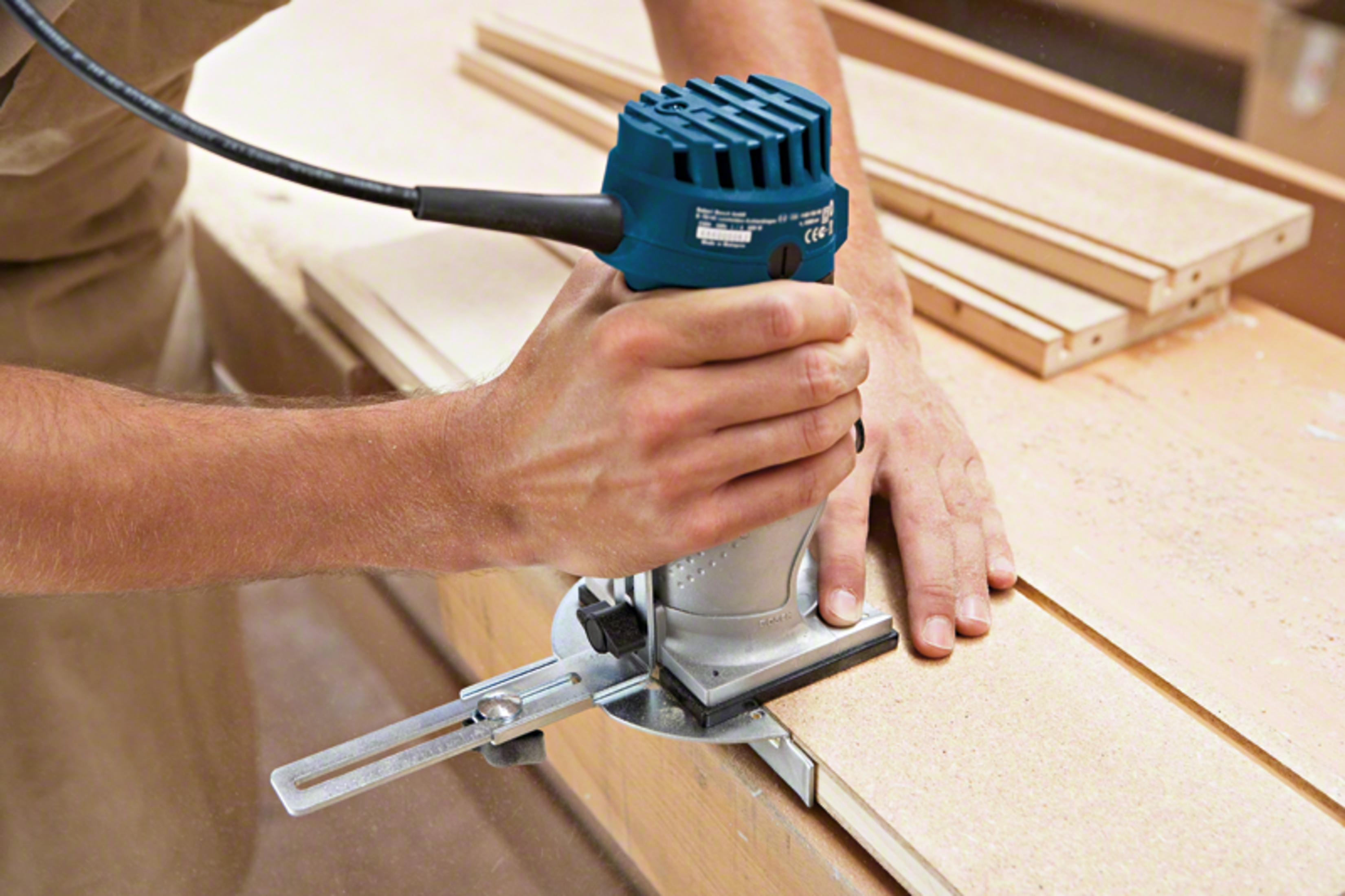 Una persona usa una fresadora eléctrica azul y plateada para dar forma a una tabla de madera.