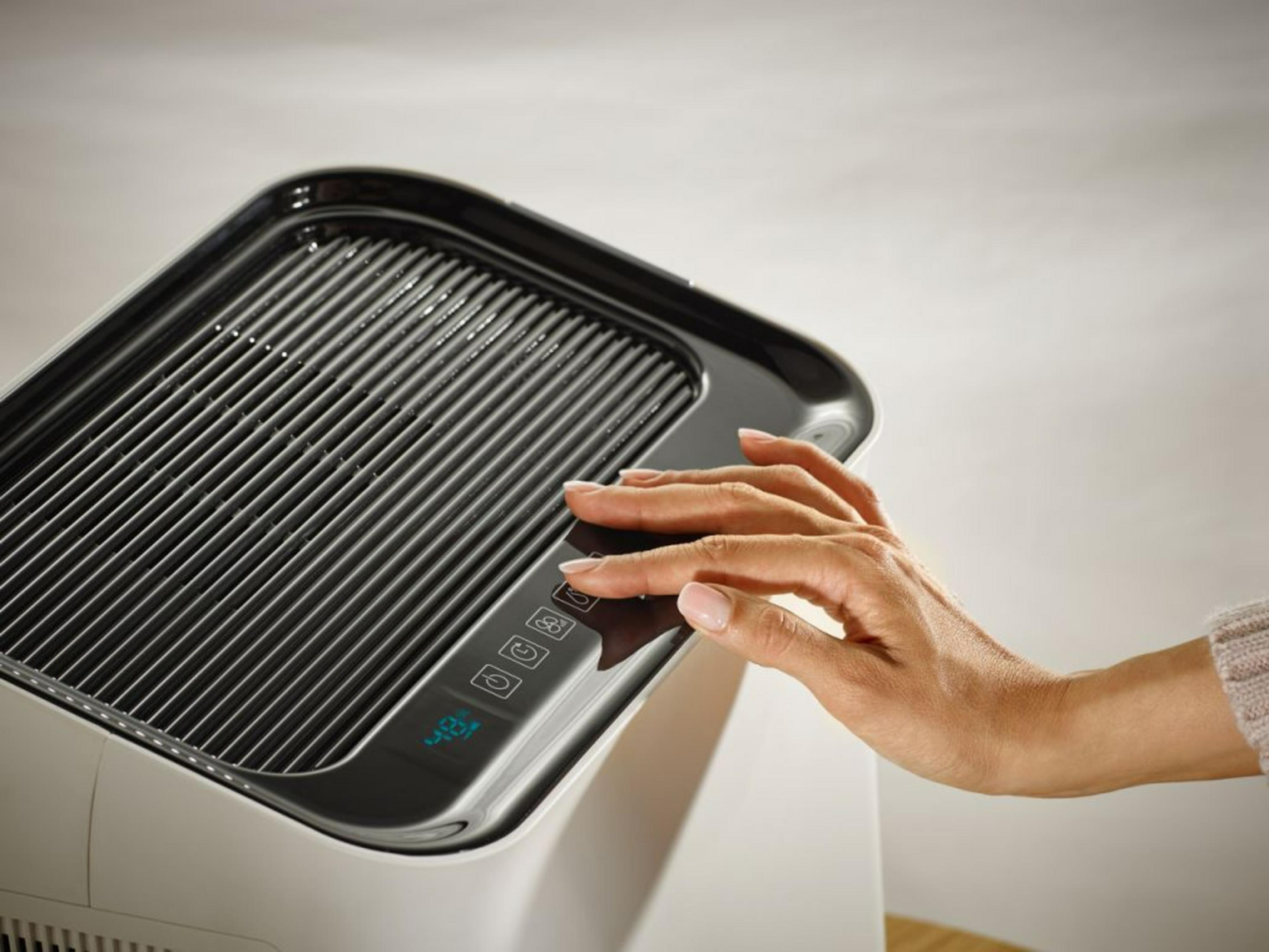 Eine Hand bedient das Touch-Bedienfeld eines weißen Luftbefeuchters mit schwarzem Grill.