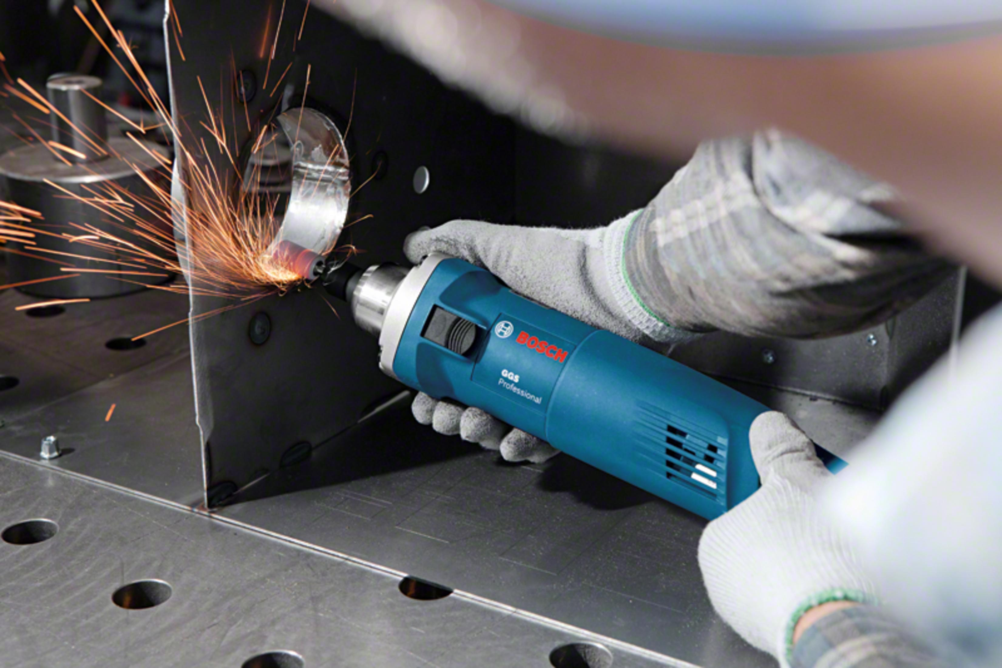 Un trabajador con guantes usa una amoladora azul Bosch en una placa de metal, creando chispas naranjas.