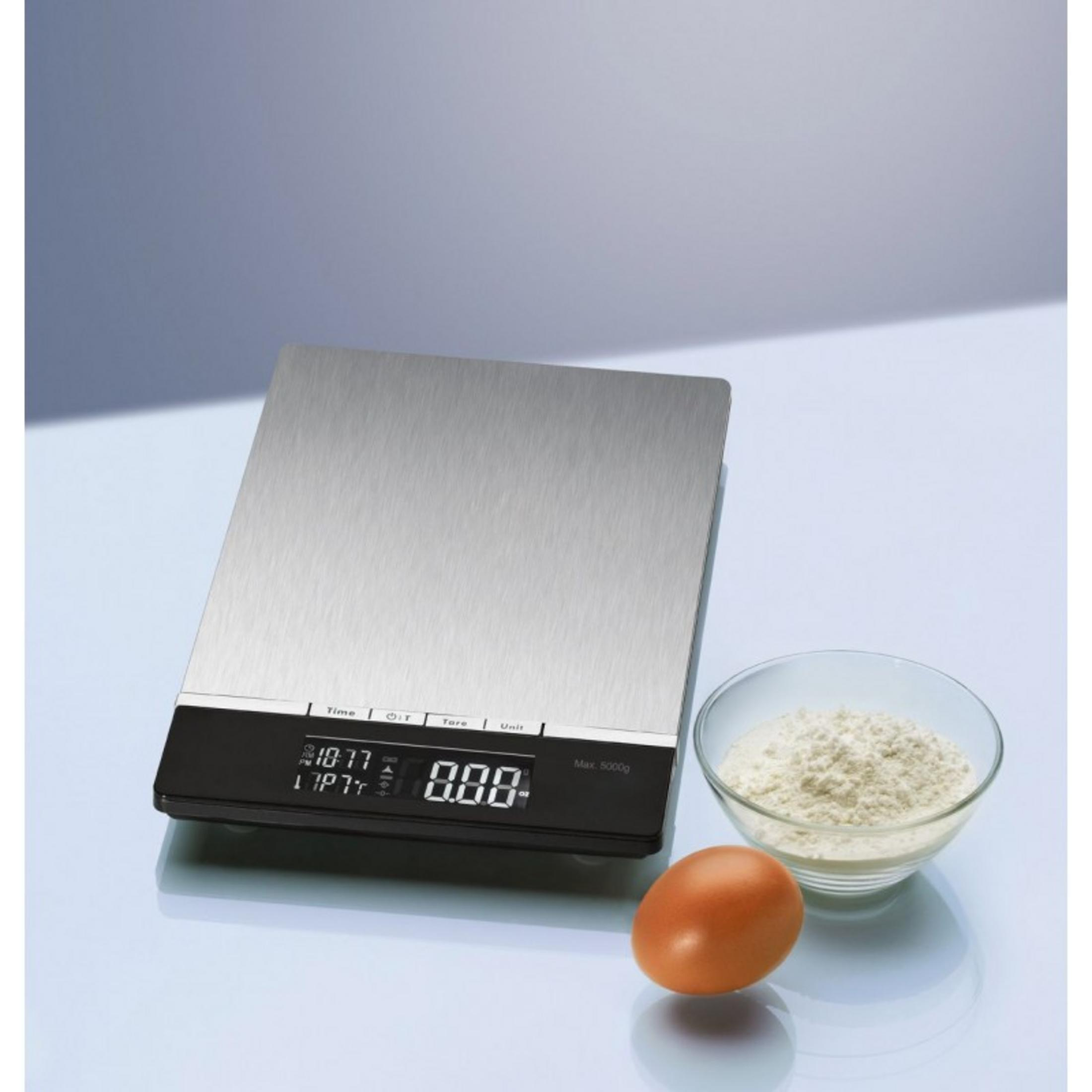 Balanza de cocina digital de acero inoxidable con pantalla, al lado un bol con harina y un huevo.
