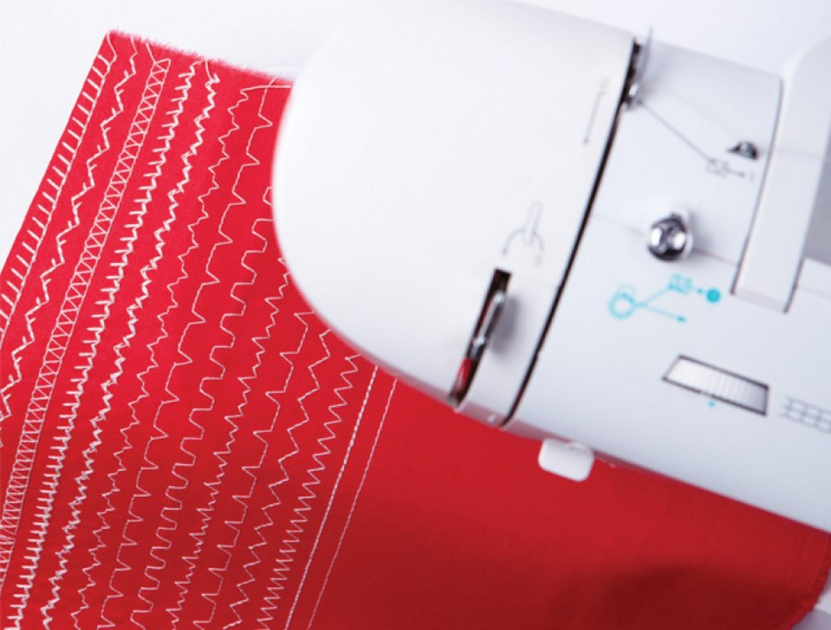 Una máquina de coser blanca cose varios patrones decorativos blancos en tela roja brillante.