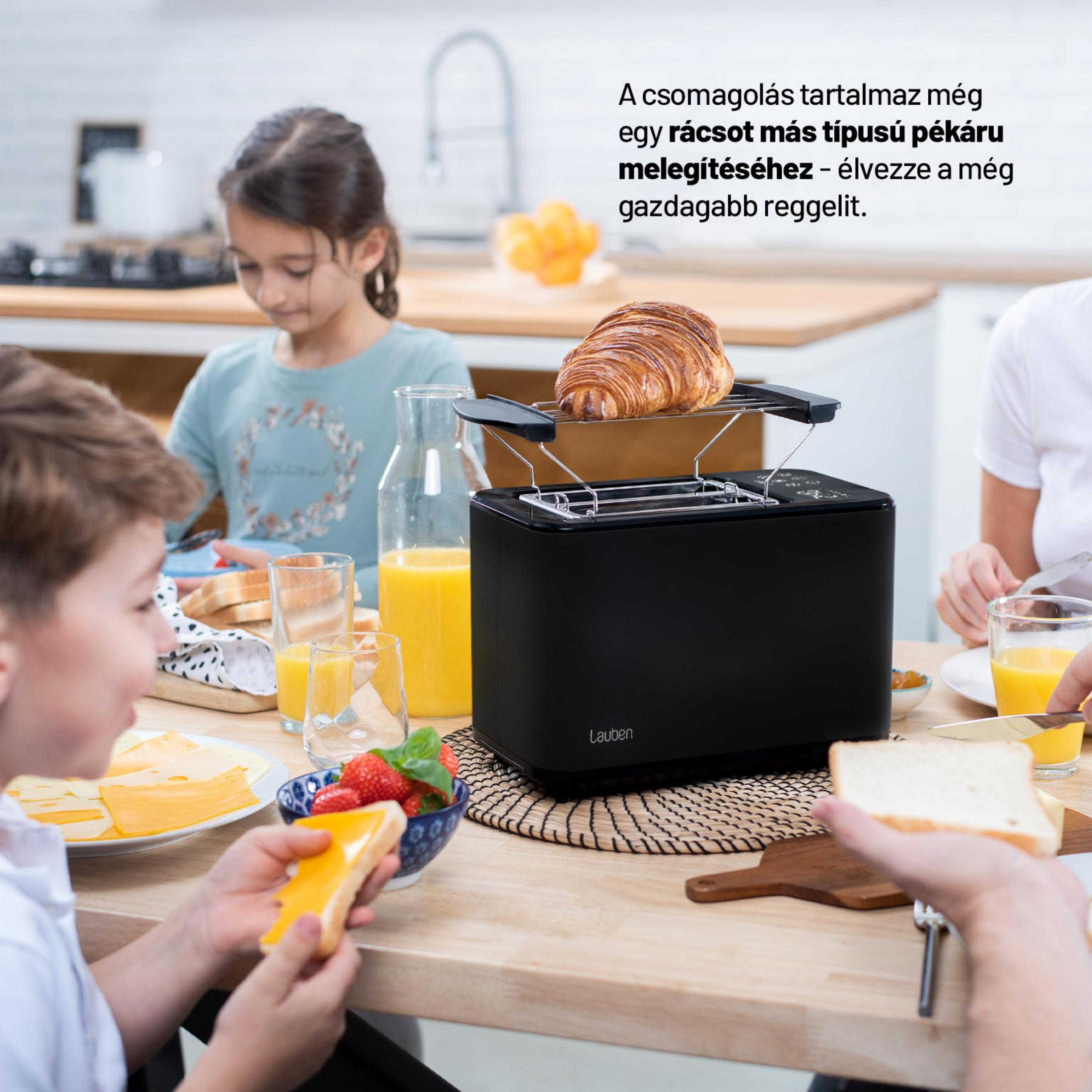Familie frühstückt am Tisch mit einem schwarzen Toaster, auf dem ein Croissant aufgewärmt wird.