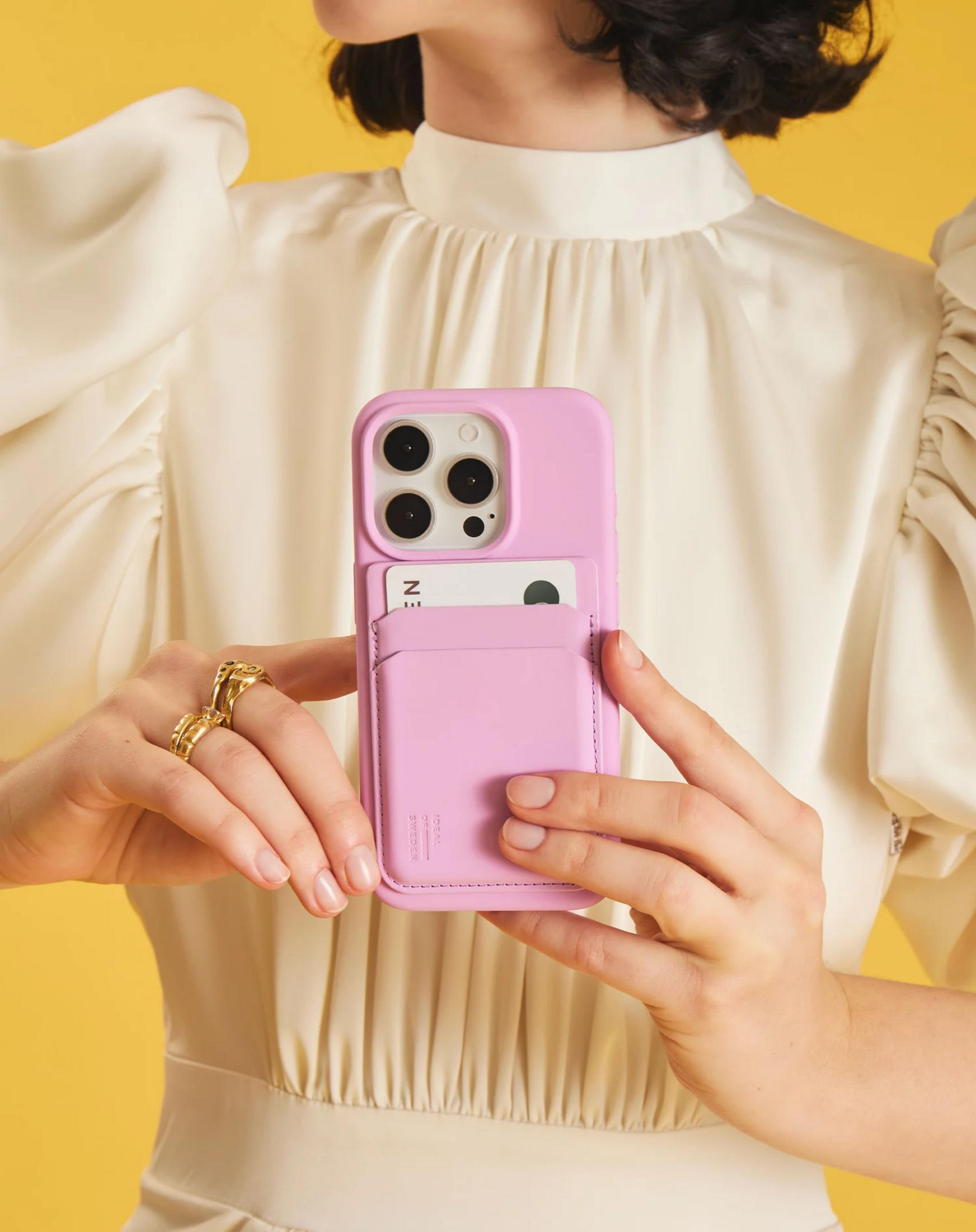 Eine Frau in weißem Kleid hält ein rosafarbenes Smartphone mit Kartenhalter vor sich.