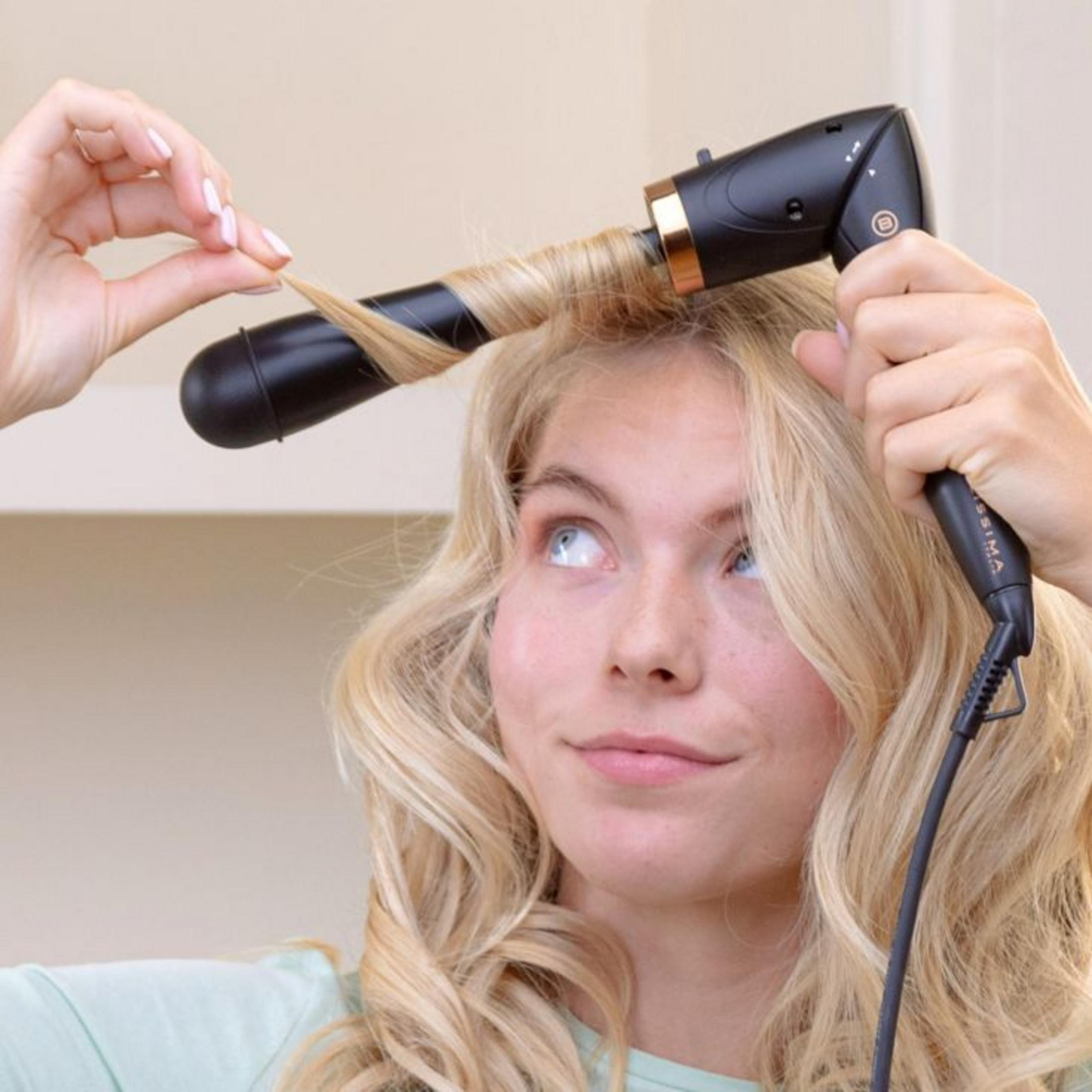 Una donna bionda avvolge una ciocca di capelli attorno a un ferro arricciacapelli nero.