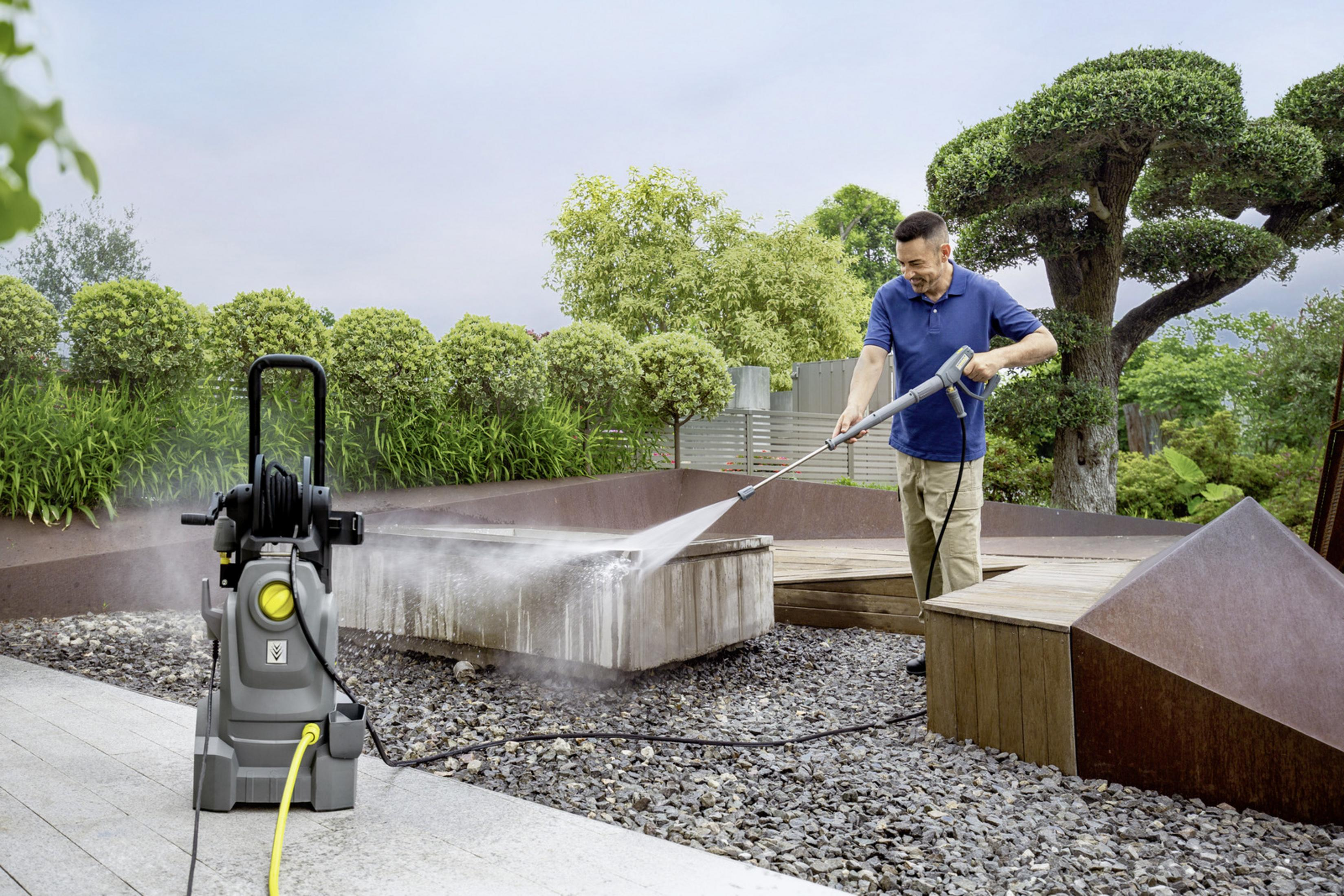 Ein Mann reinigt eine Steinmauer in einem Garten mit einem grauen Hochdruckreiniger.