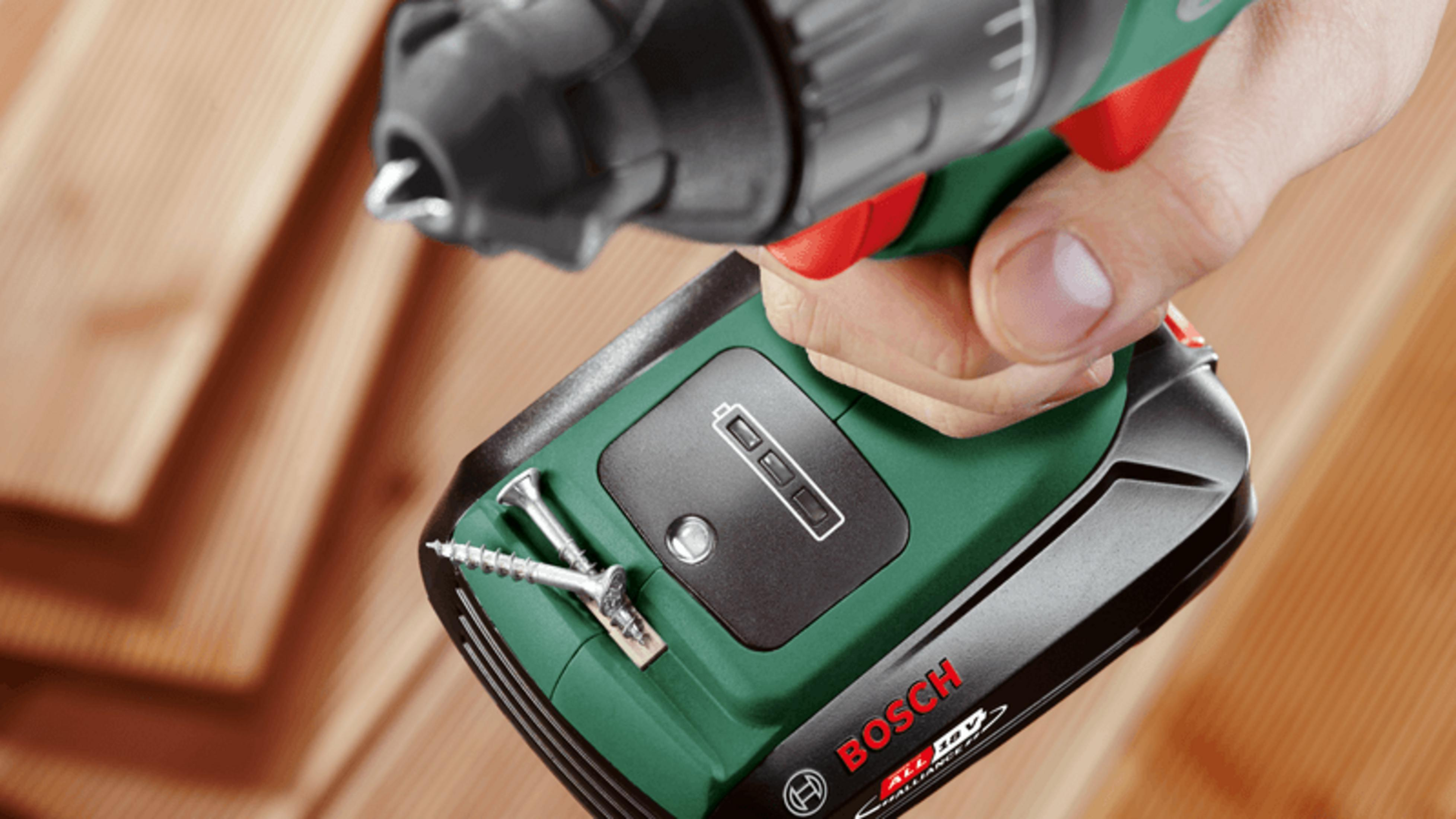 Un trapano a batteria verde Bosch con indicatore di carica è tenuto sopra assi di legno.