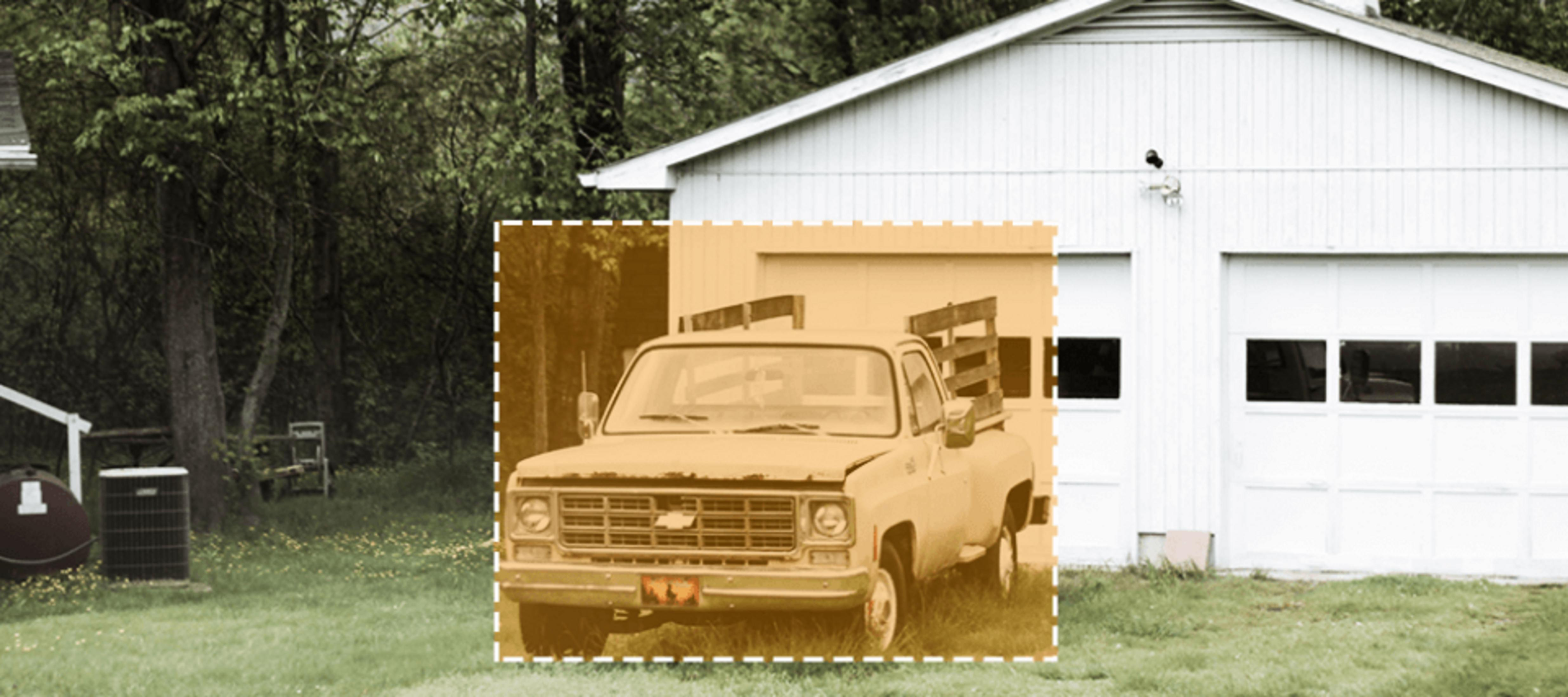 Ein alter Pickup-Truck parkt auf dem Gras vor einer weißen Garage.