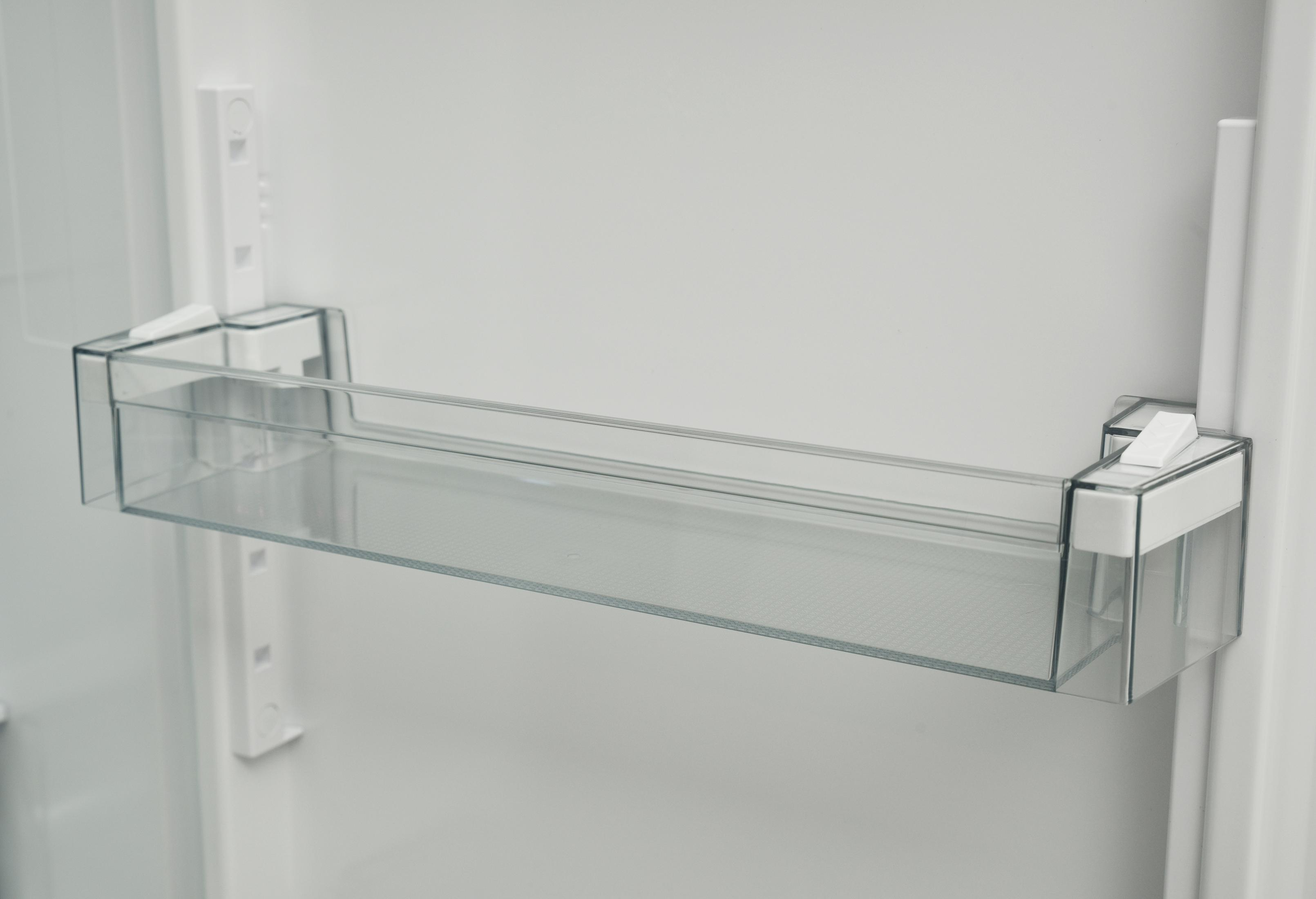Un ripiano in plastica trasparente vuoto all'interno della porta di un frigorifero bianco.