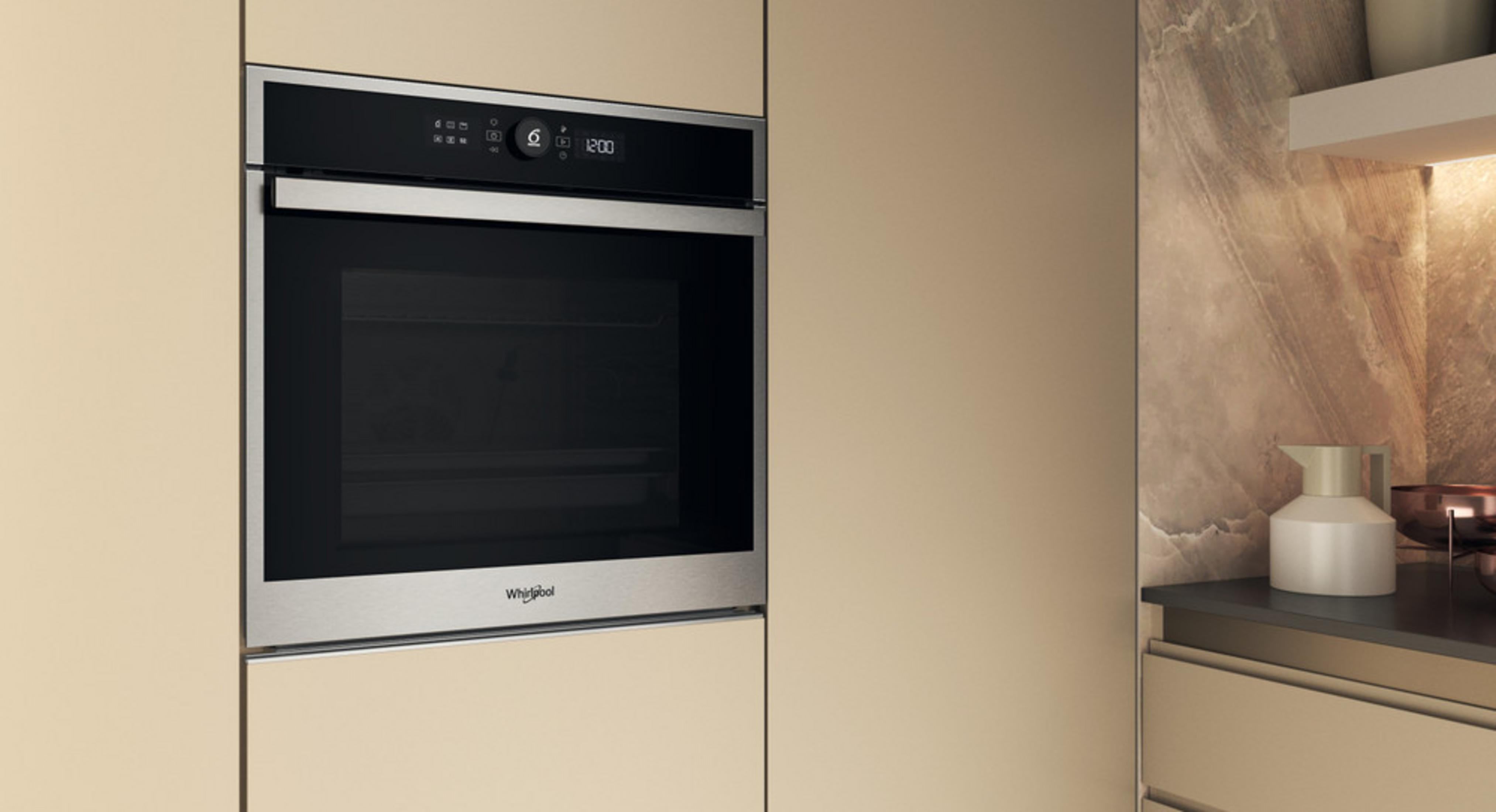 Un horno Whirlpool moderno empotrado con pantalla digital y detalles de acero inoxidable en una pared de cocina beige.