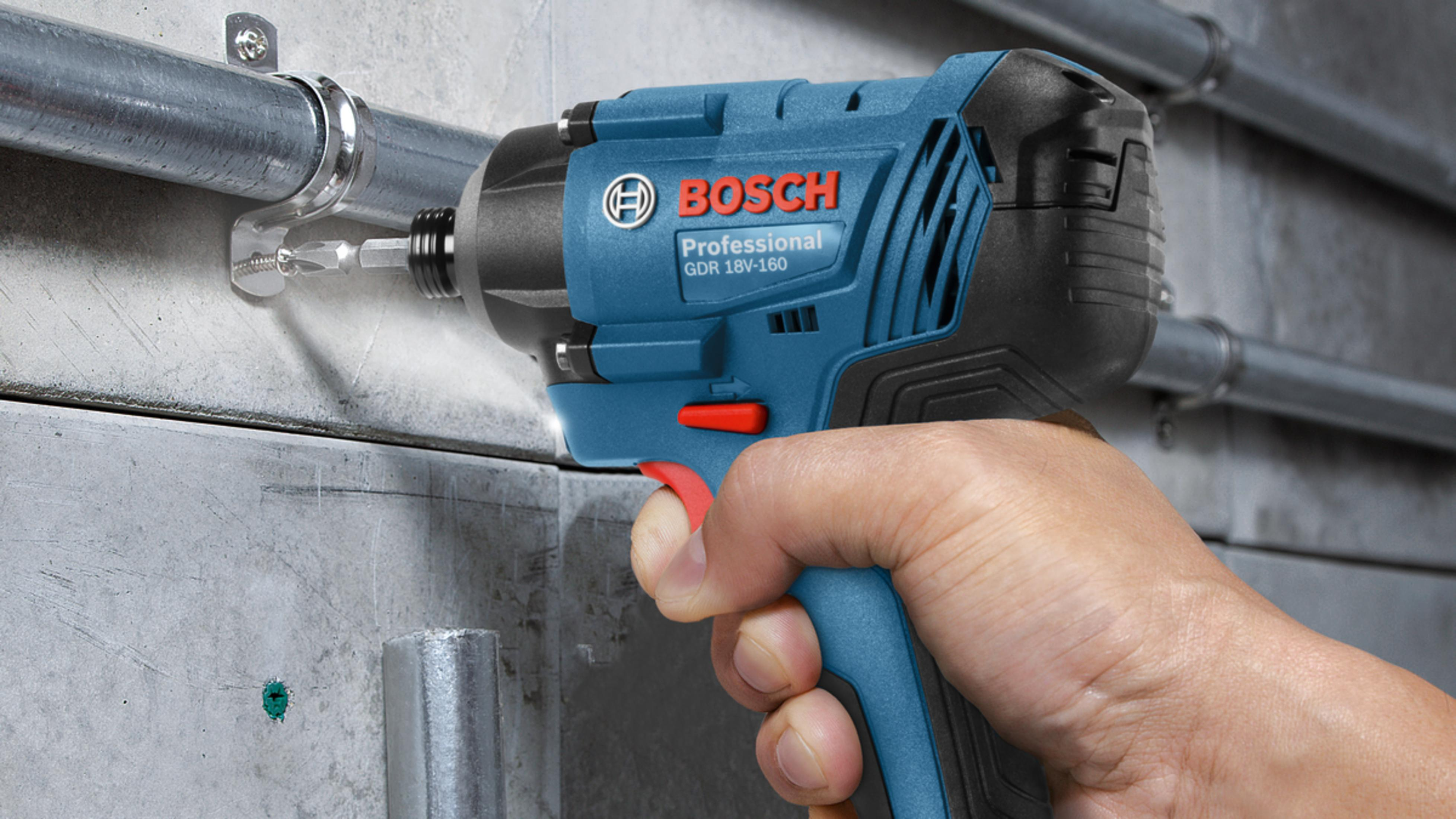 Bir el, metal duvara vida vuran mavi bir Bosch akülü darbeli matkap tutuyor.