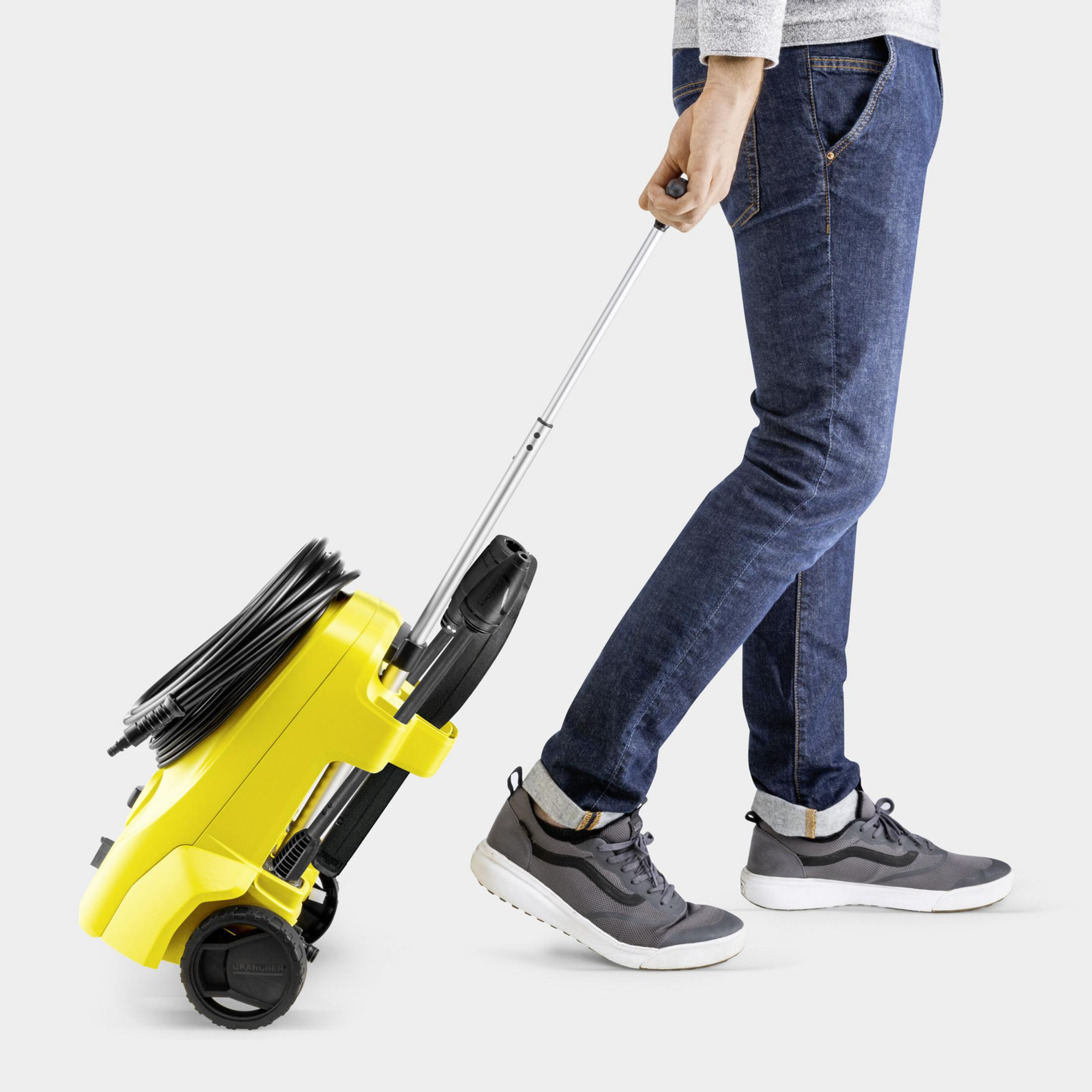 Eine Person in Jeans und Turnschuhen zieht einen gelb-schwarzen Hochdruckreiniger auf Rädern an dessen Teleskopstange.