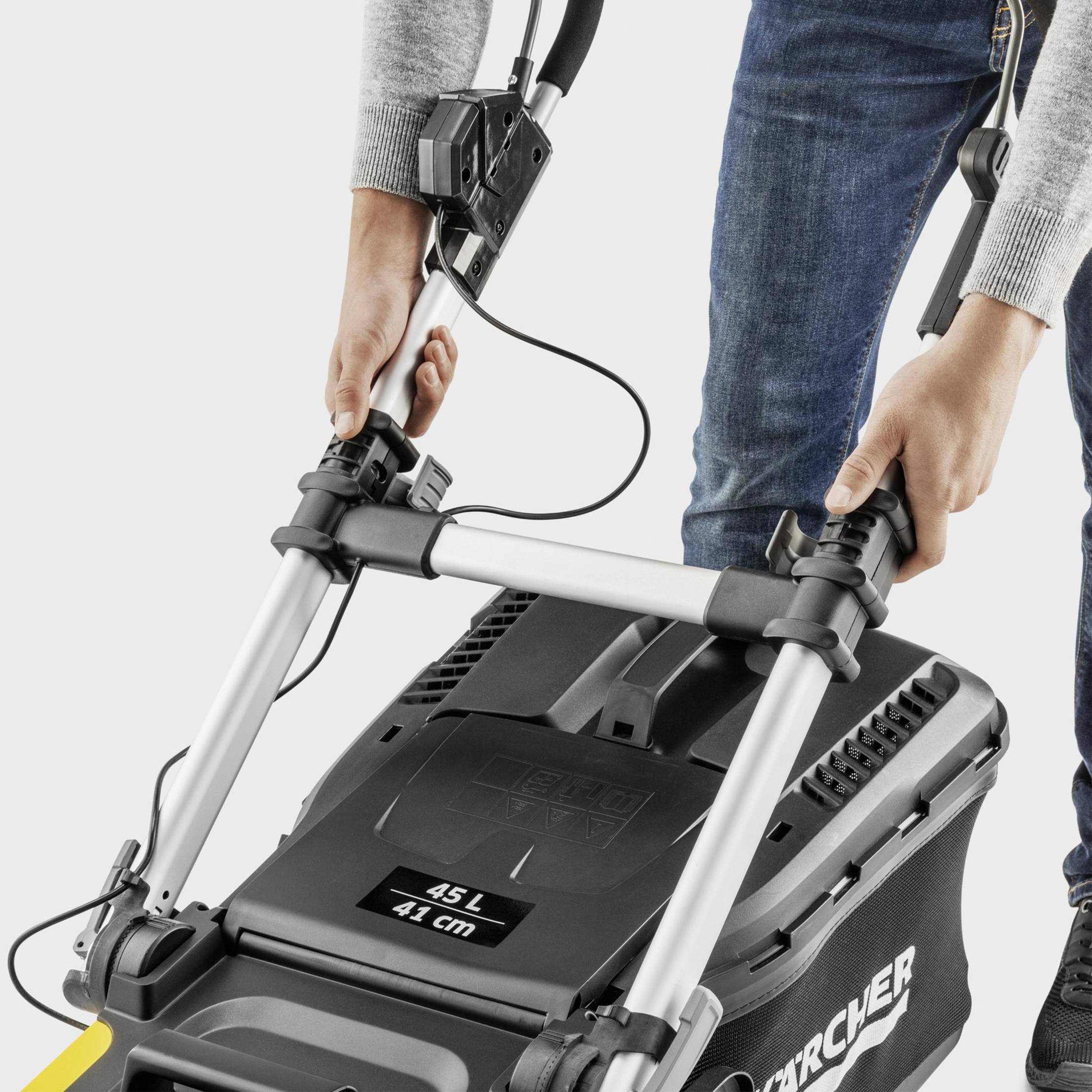 Eine Person in Jeans und grauem Pullover hält die Griffe eines schwarzen Rasenmähers mit 45-Liter-Fangbox.