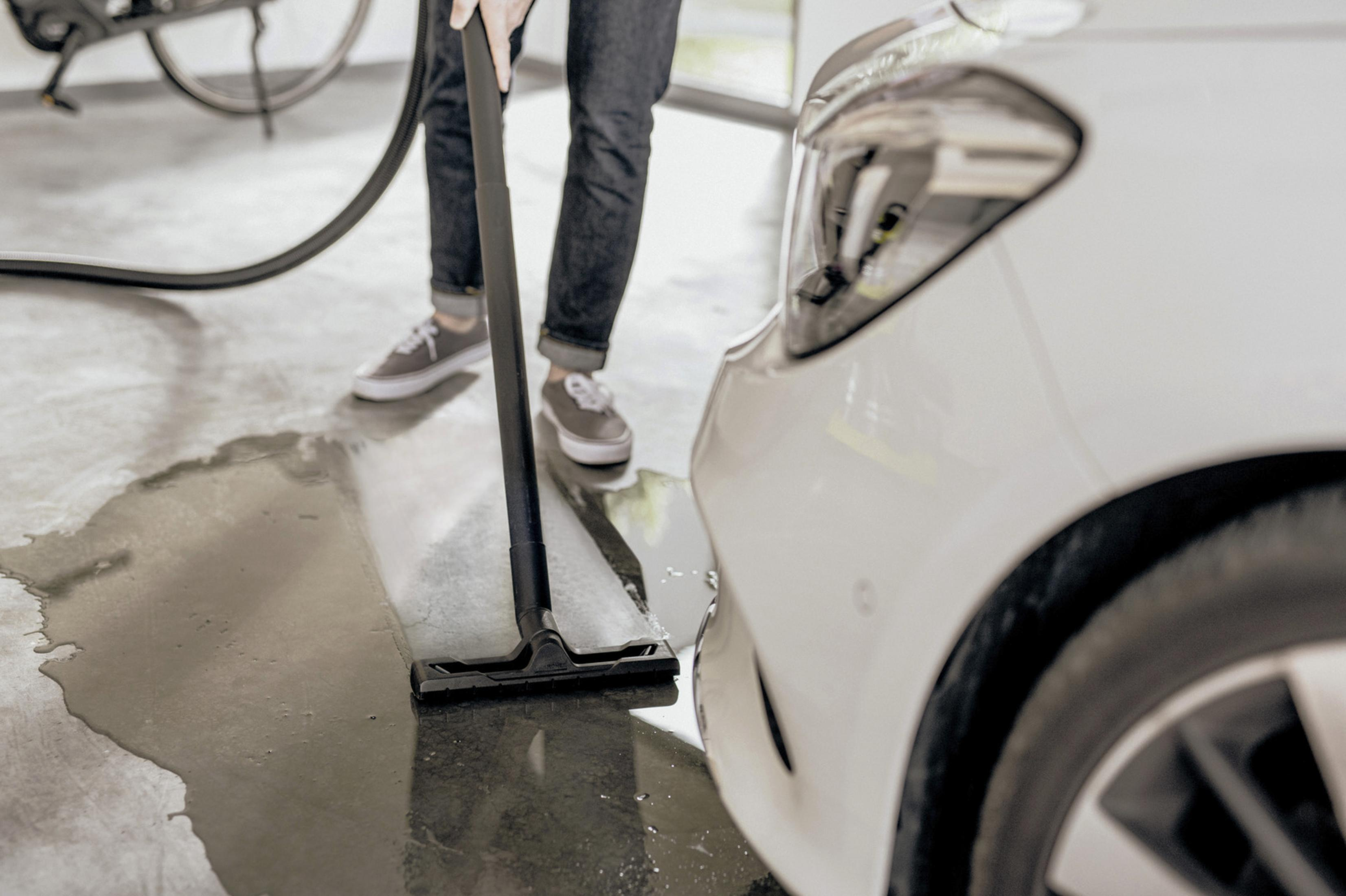 Eine Person benutzt einen Wassersauger auf dem Boden neben einem weißen Auto.