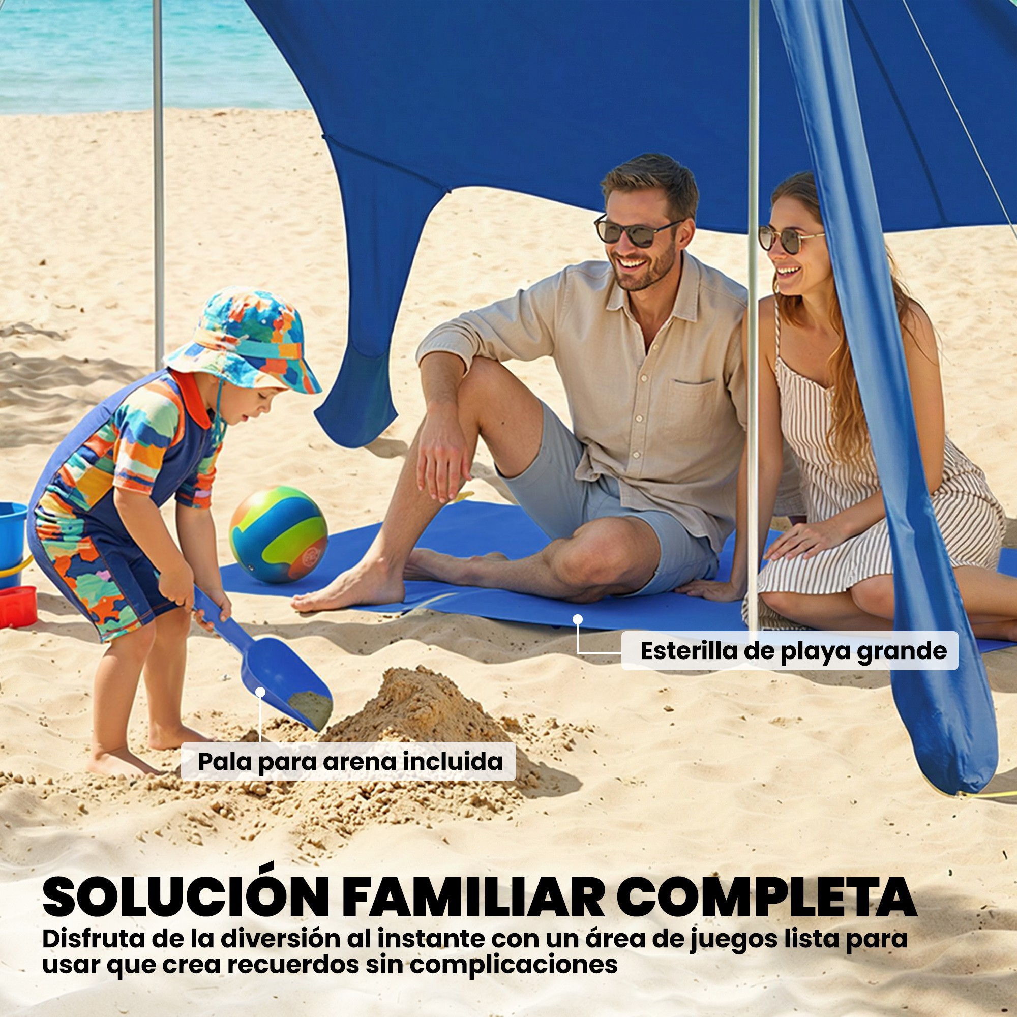 Una famiglia siede in spiaggia sotto un ombrellone blu, un bambino gioca con la sabbia e una paletta.