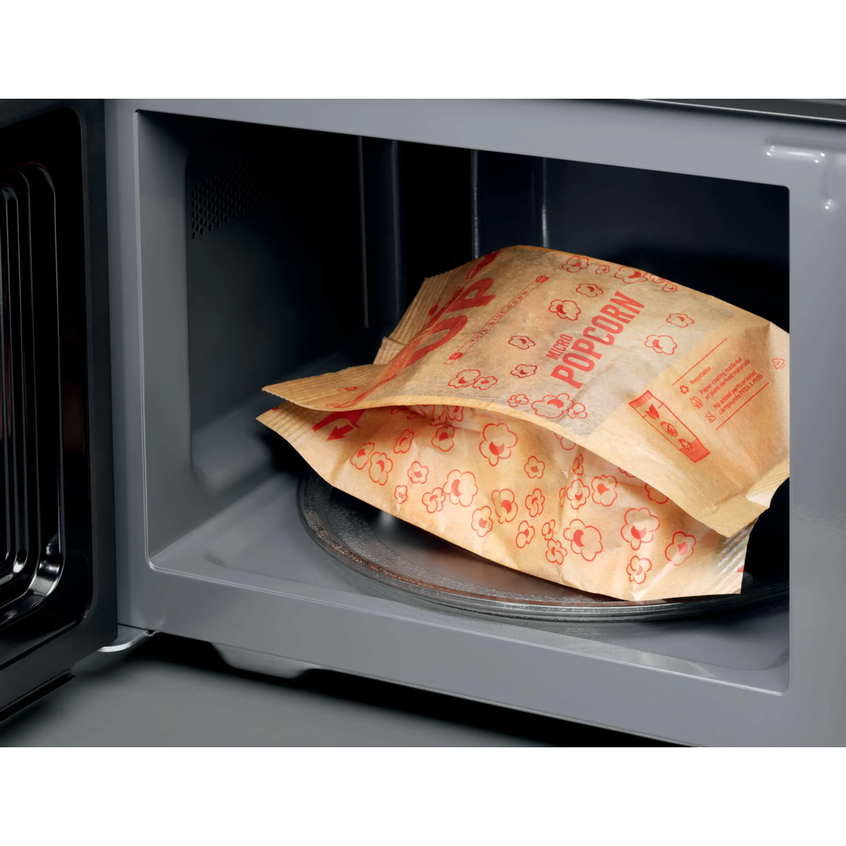 Una bolsa de papel de palomitas para microondas sin abrir descansa sobre el plato giratorio de un microondas gris.