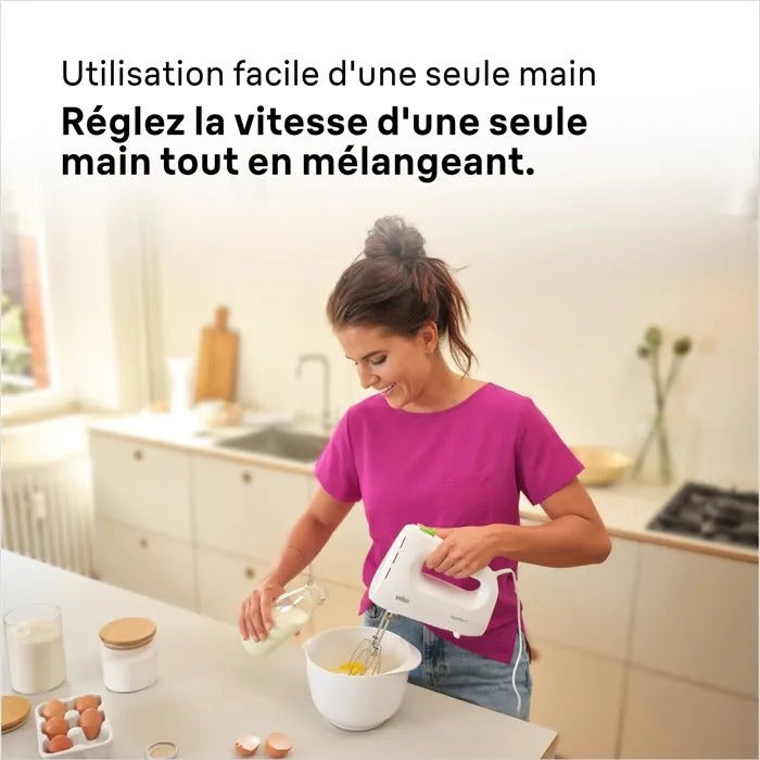 Eine Frau in einem pinken Shirt mixt mit einer Hand Teig und gießt Milch hinzu.