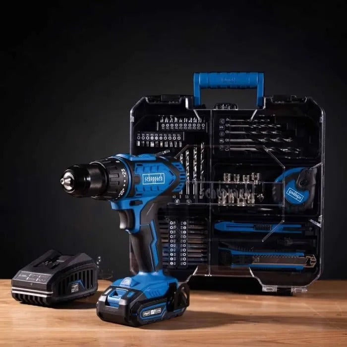Taladro inalámbrico azul, cargador y caja de herramientas sobre una superficie de madera.