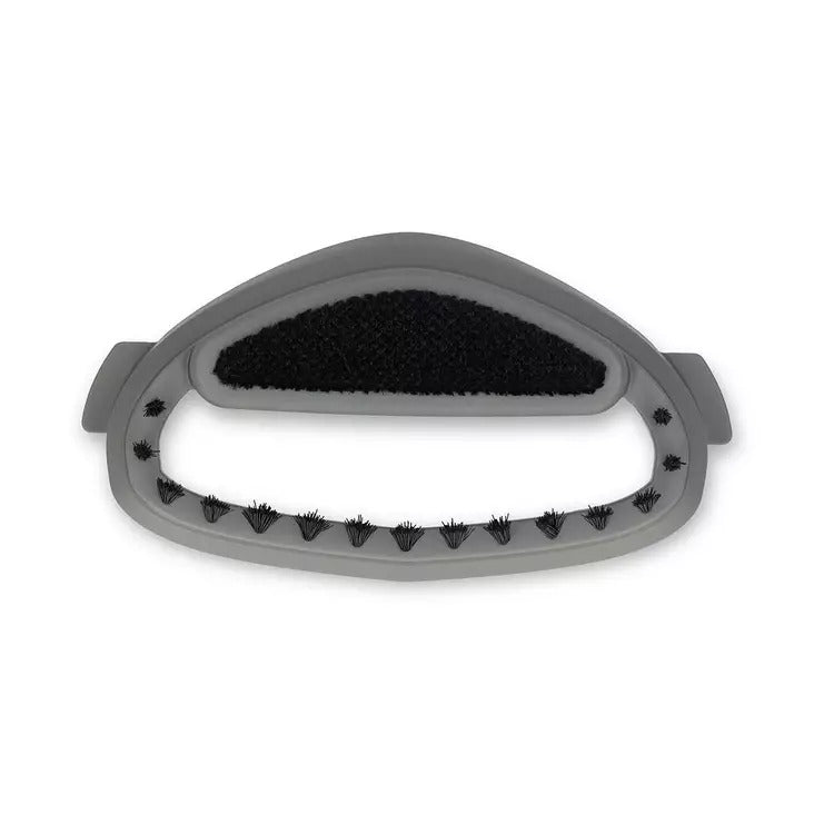 Accessore per stiratura a vapore in plastica grigia con setole curve e cuscinetto anti-pelucchi su sfondo bianco.